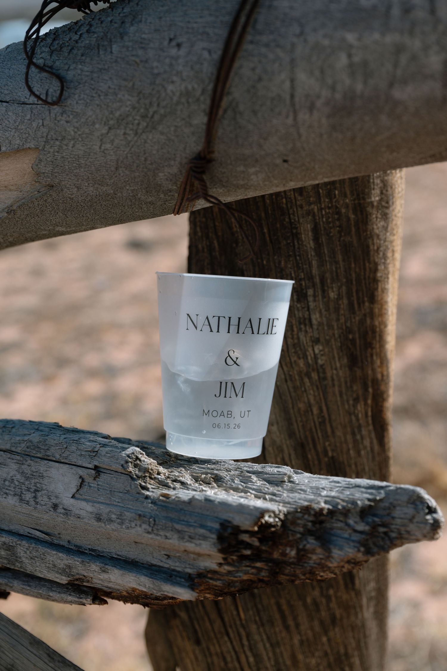 Custom frosted cup for Nathalie and Jim wedding in Moab UT balanced on rustic wooden fence post.