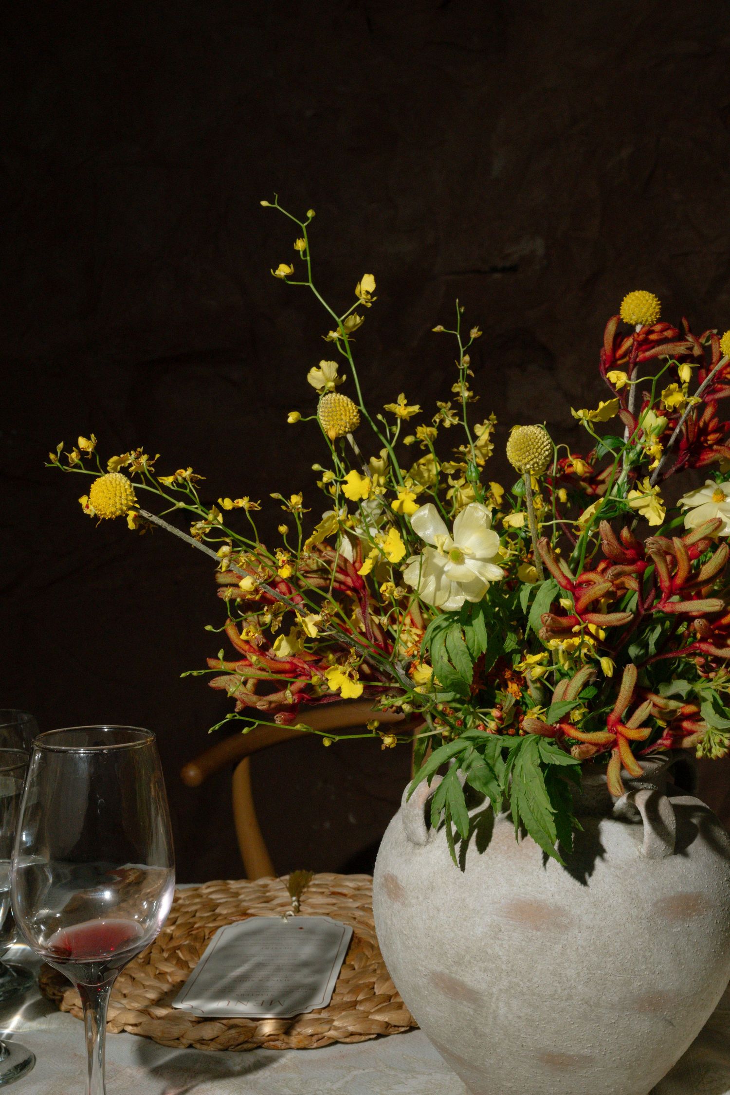 Rustic ceramic vase with yellow wildflowers and red peppers on a candlelit wedding reception table.