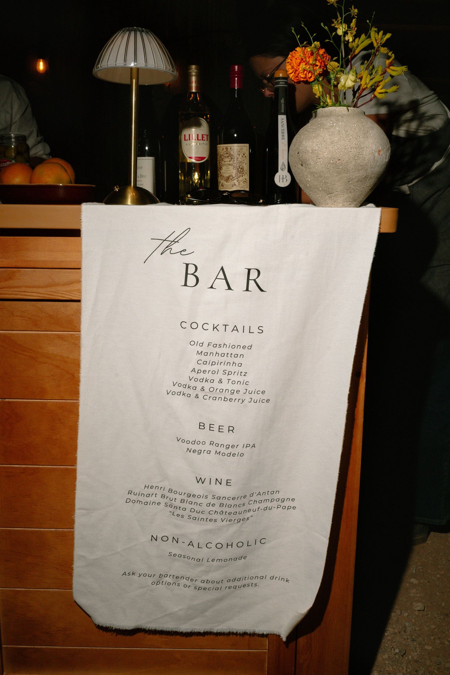Elegant fabric bar menu sign listing cocktails, beer, wine, and non-alcoholic options at a wedding reception.