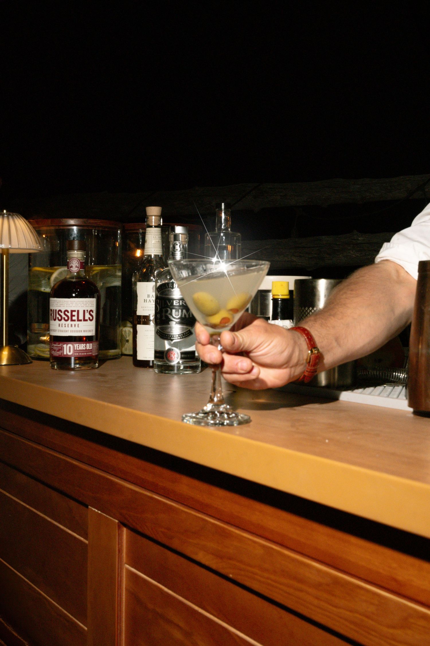 Bartender presenting a sparkling martini cocktail on a polished wooden bar at a wedding reception.