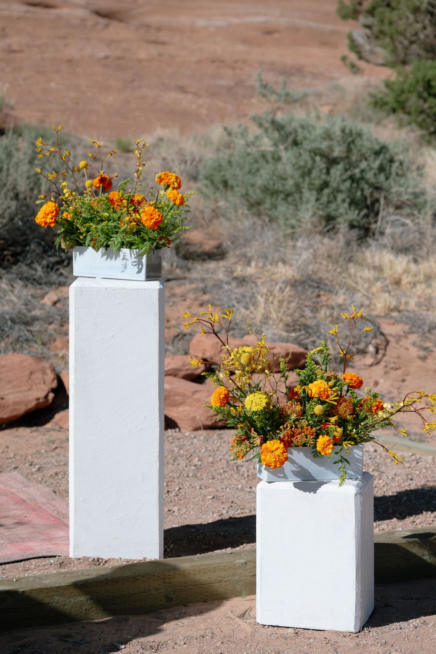Two white pedestals with vibrant orange marigold floral arrangements at desert wedding in Moab Utah.