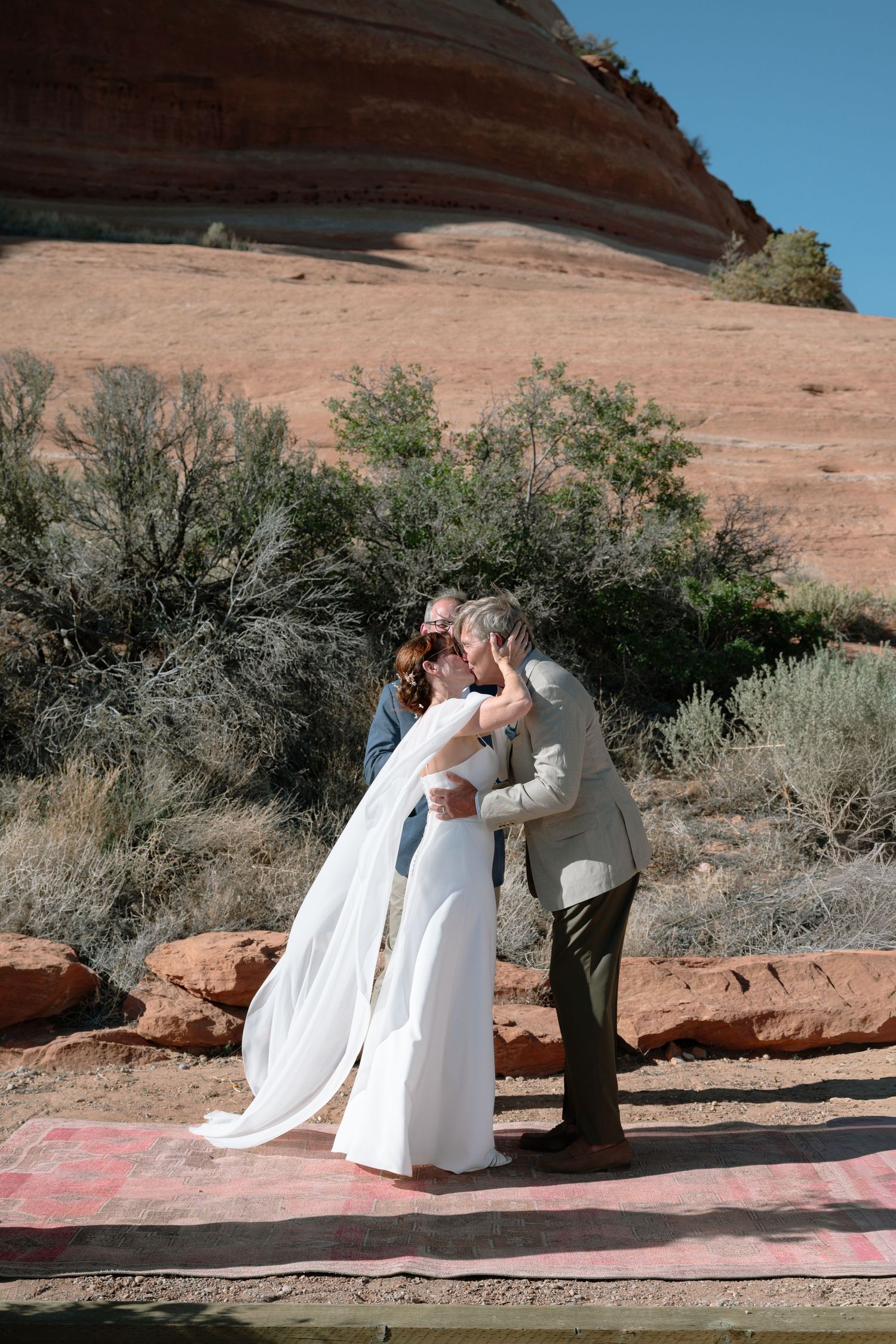 Bride and groom share first kiss at outdoor desert wedding ceremony with red rock formations in Moab Utah.