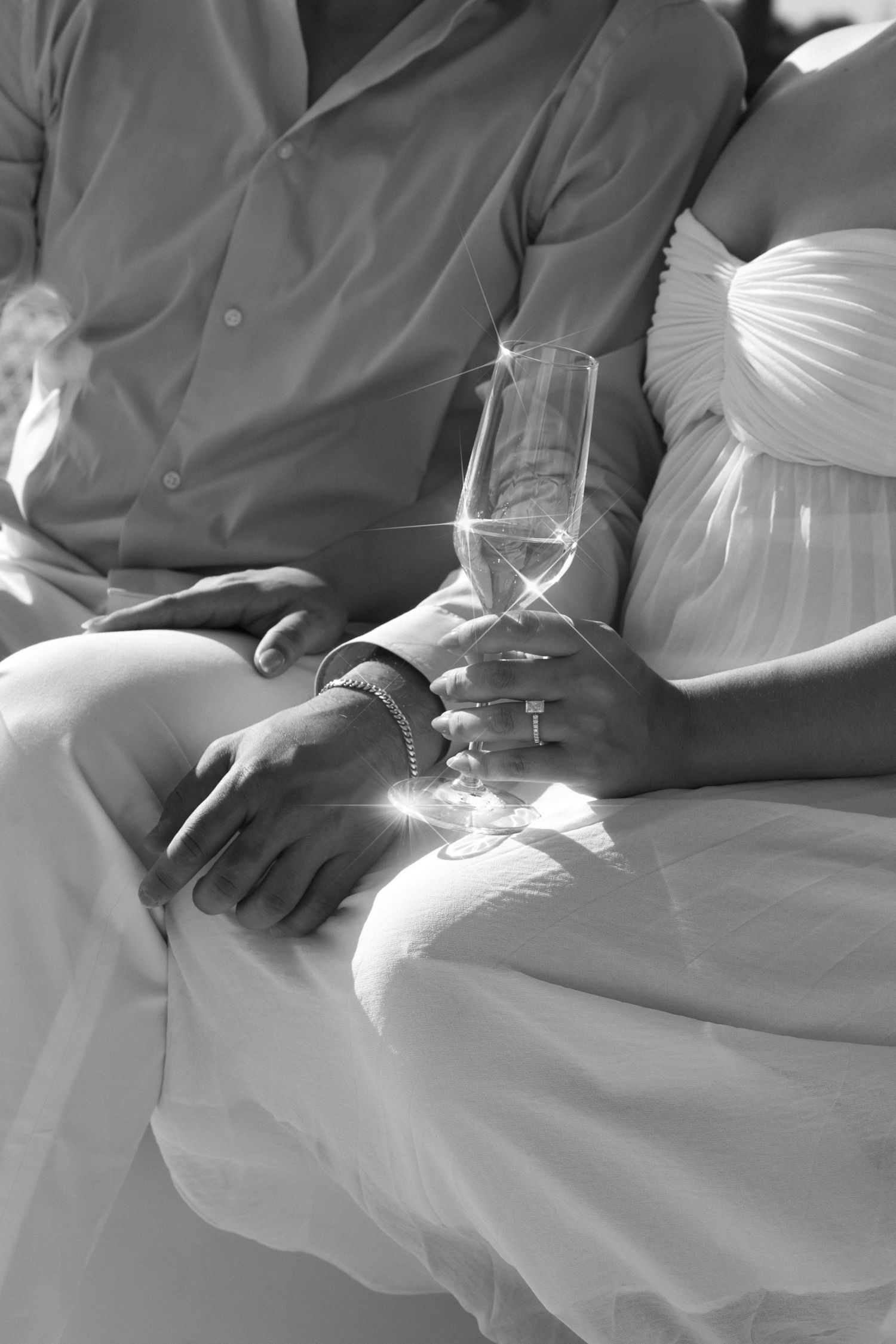 Black and white close-up of a couple holding a sparkling champagne flute, with the woman in a white dress and man in a gray shirt.