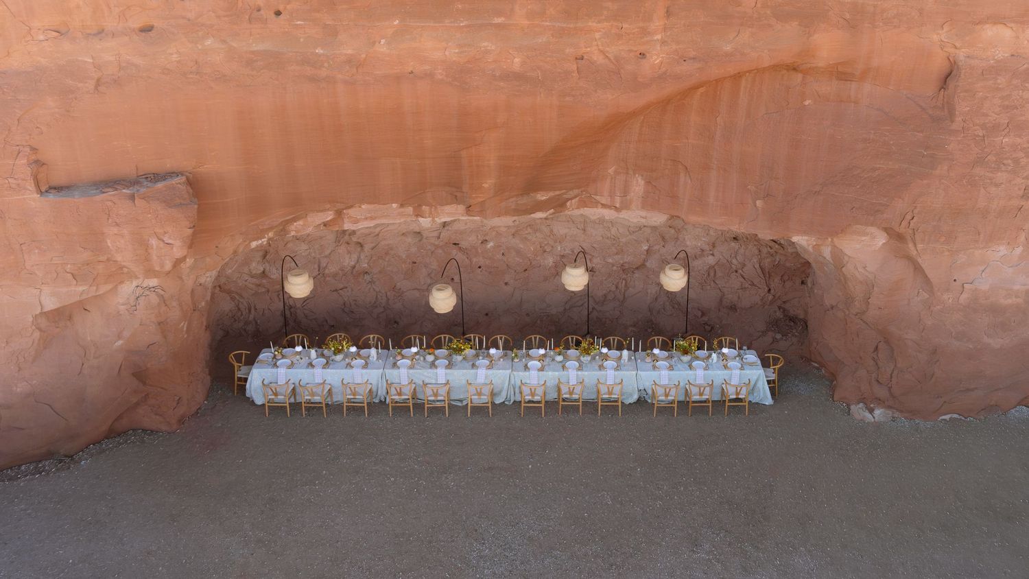 Elegant outdoor dining table set under a red sandstone rock arch in a desert canyon setting.