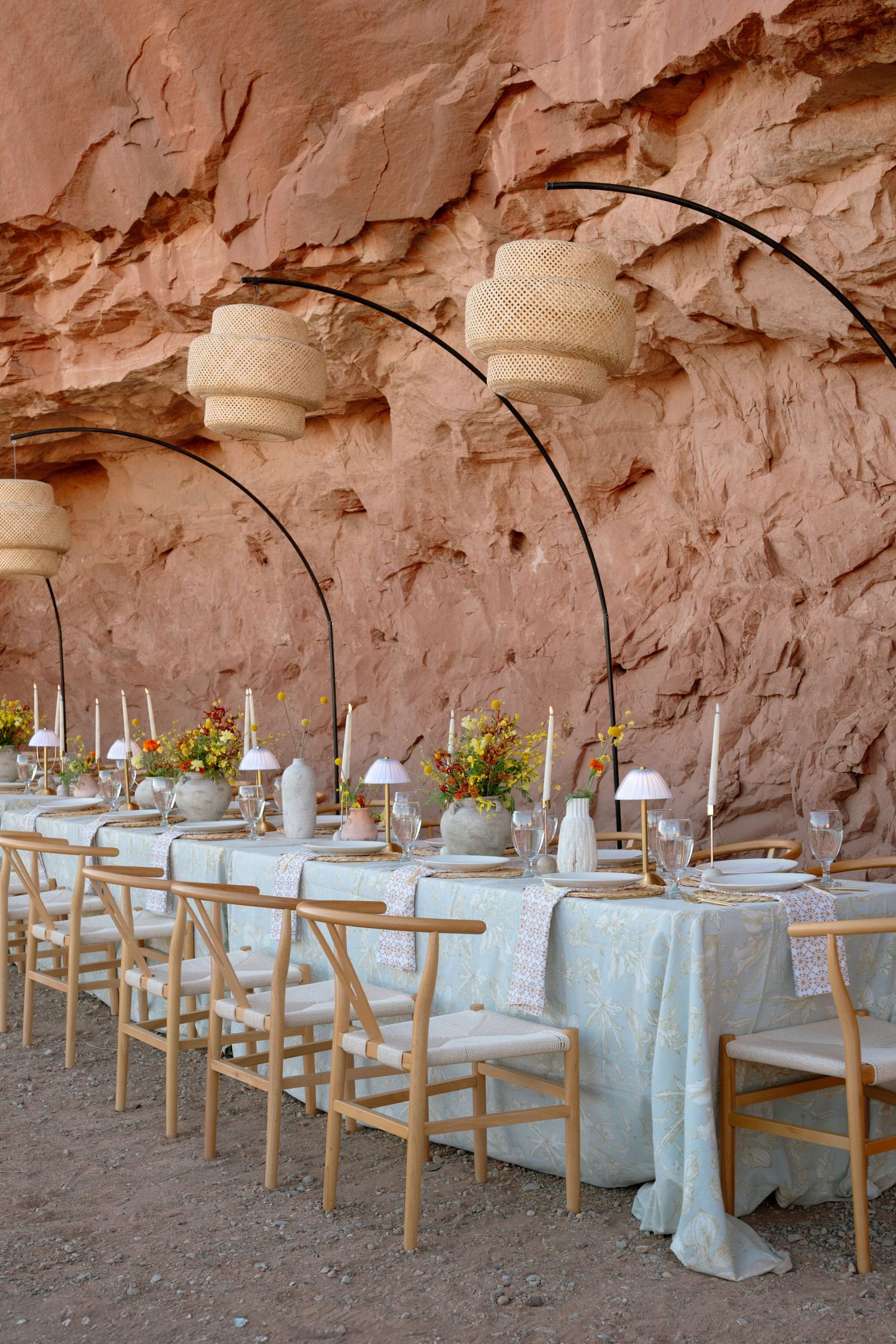 Long elegant wedding reception table set against a stunning red sandstone canyon wall with wicker pendant lights.