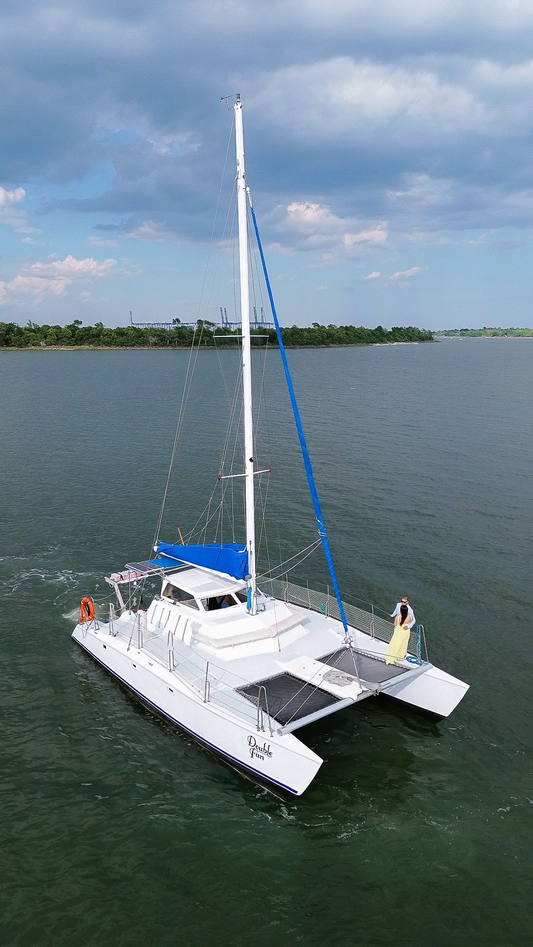 White catamaran sailboat with blue accents sailing on calm green waters under a partly cloudy sky.