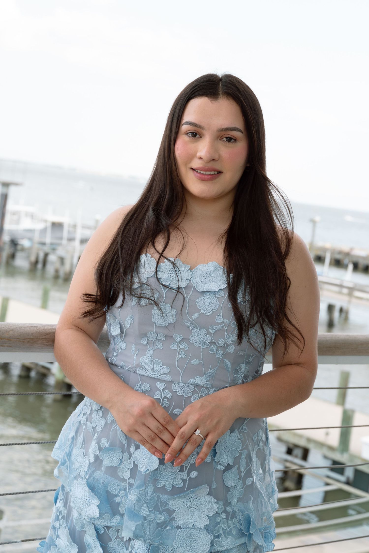 Young woman in a blue floral strapless dress posing on a waterfront dock.