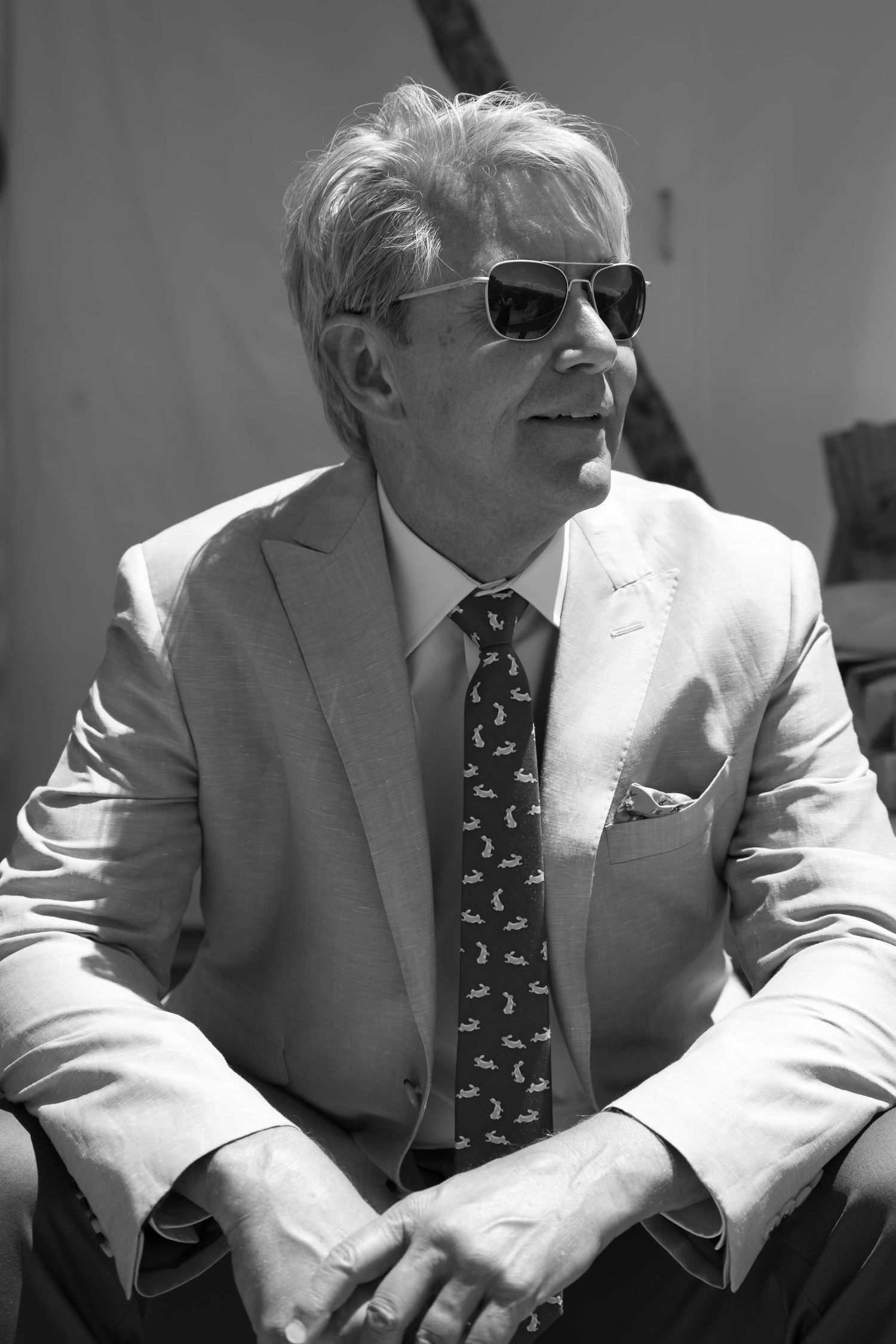 Elegant man in suit, tie, and sunglasses poses confidently in black and white portrait photo.