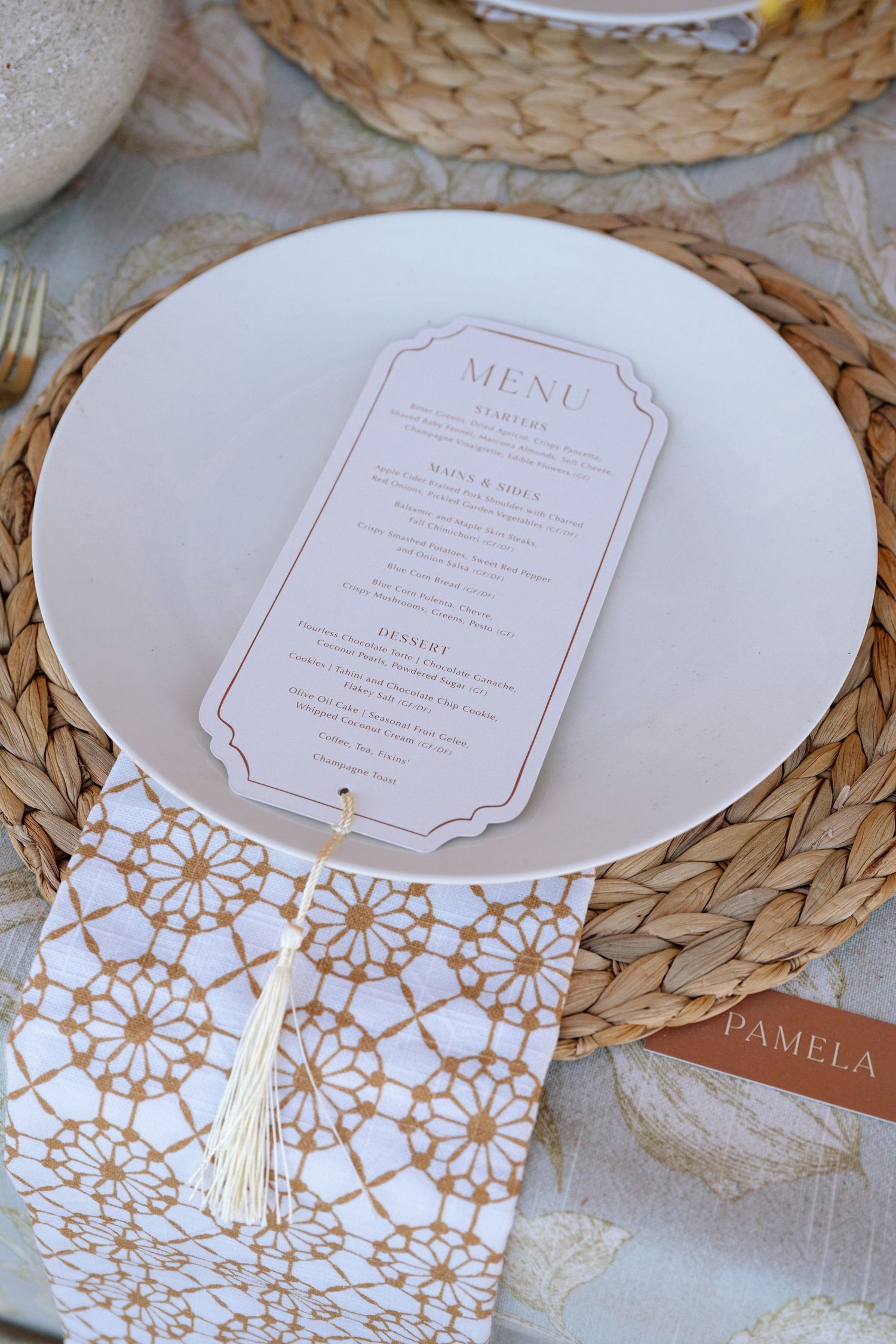 Elegant wedding place setting with a menu card, woven placemat, patterned napkin, and name card reading Pamela.