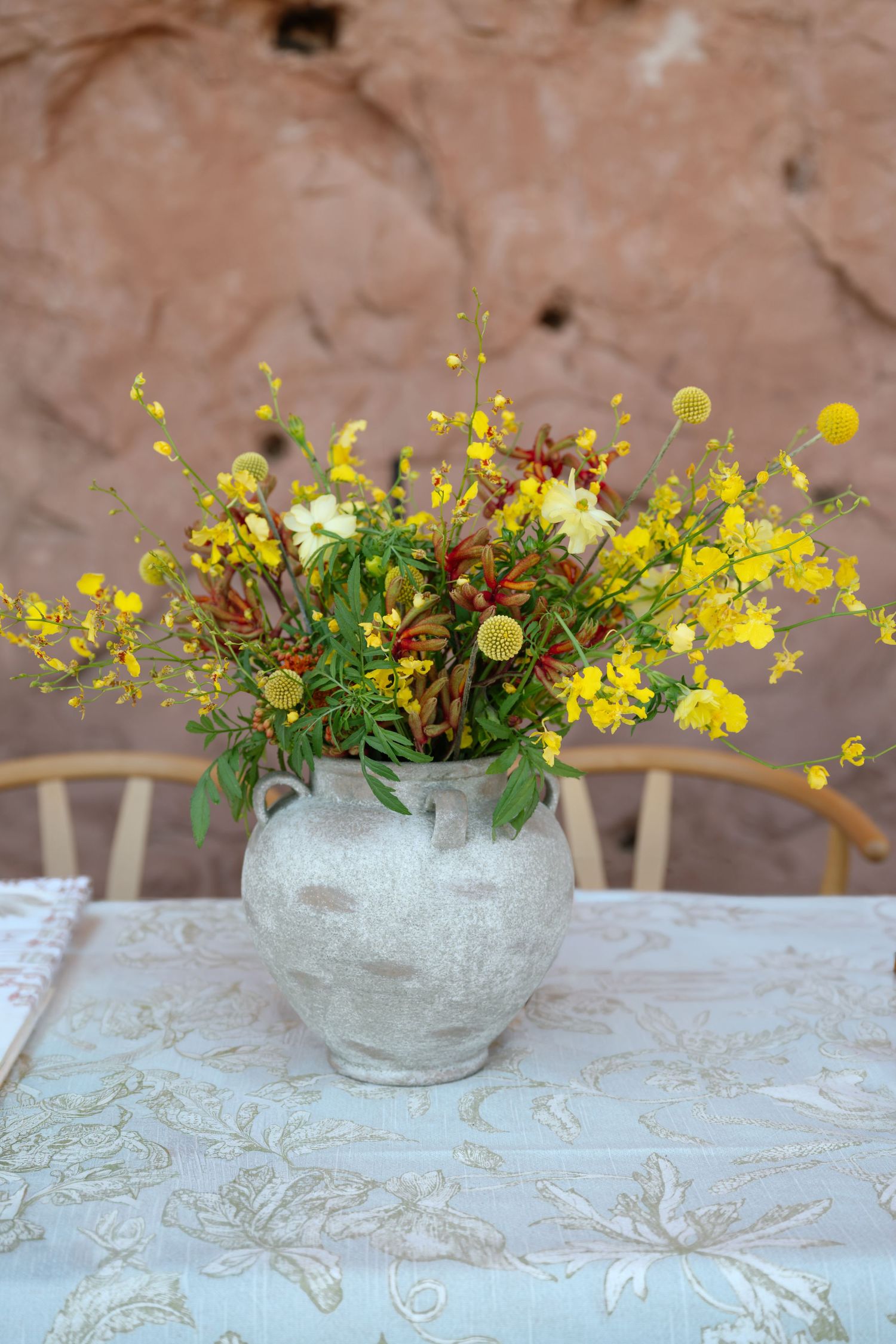 Rustic stone vase filled with yellow wildflowers and red peppers on a floral patterned wedding table.