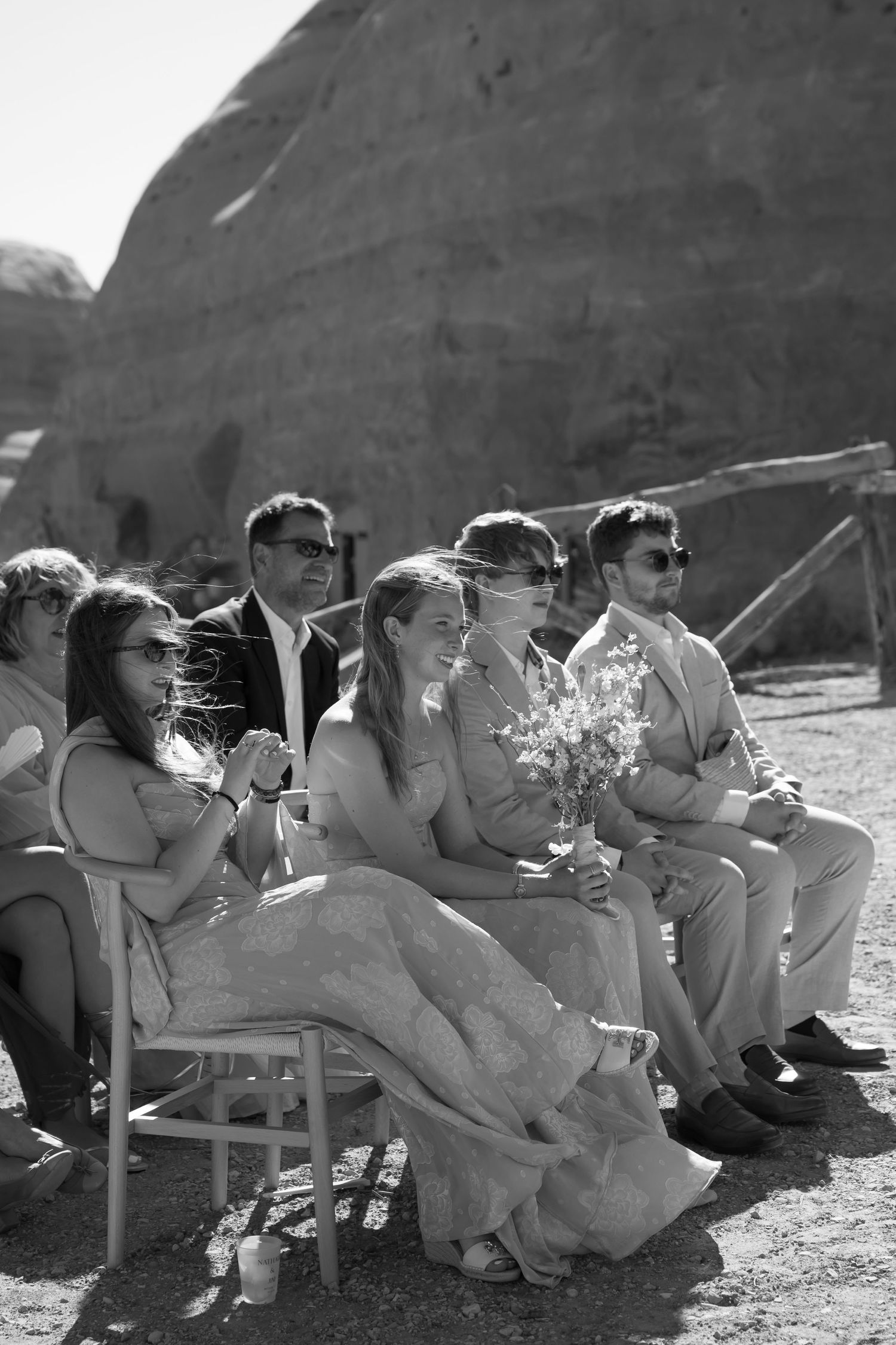 Black and white photo of wedding guests seated outdoors in desert ceremony.