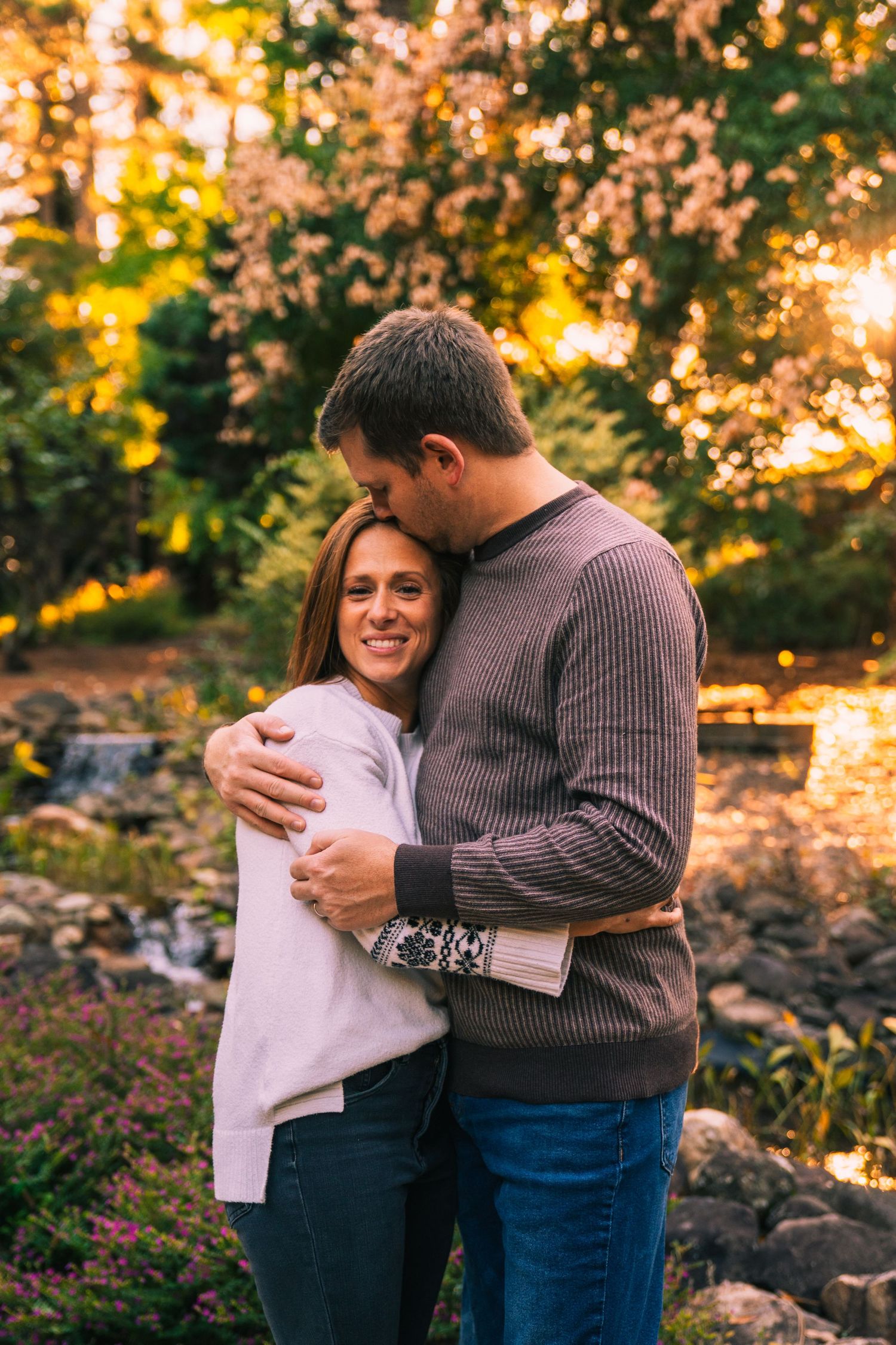 A couple embraces in a romantic autumn setting with golden sunlight filtering through trees in the background.