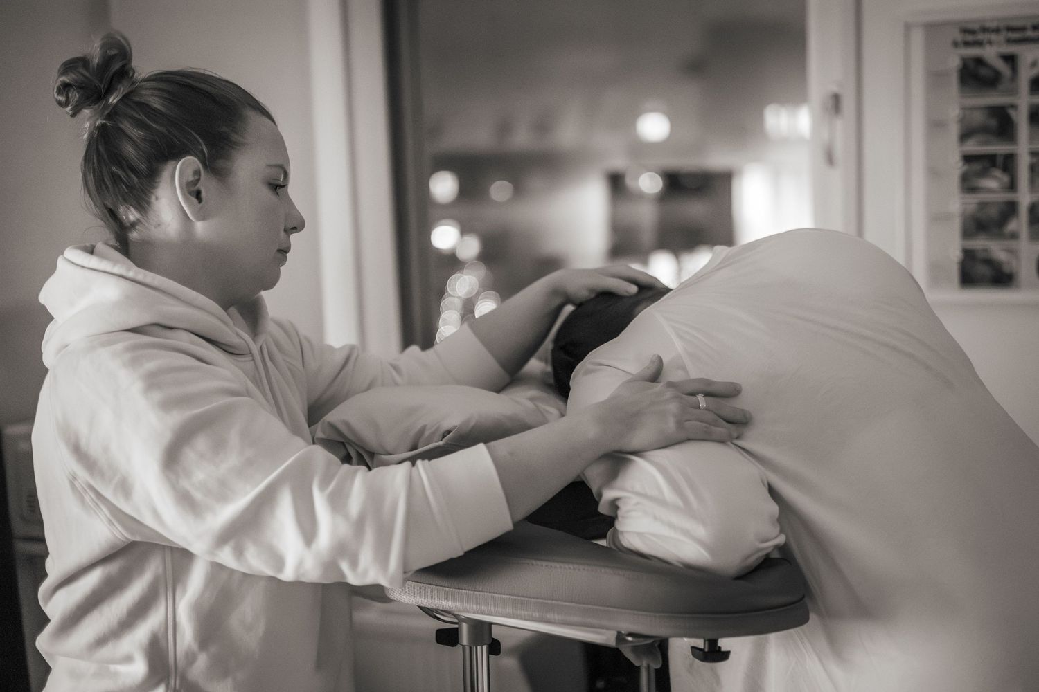 Svartvit bild på en doula som stöttar en födande kvinna och håller sina händer på huvud och arm. Förlossningsfoto, Södertälje sjukhus
