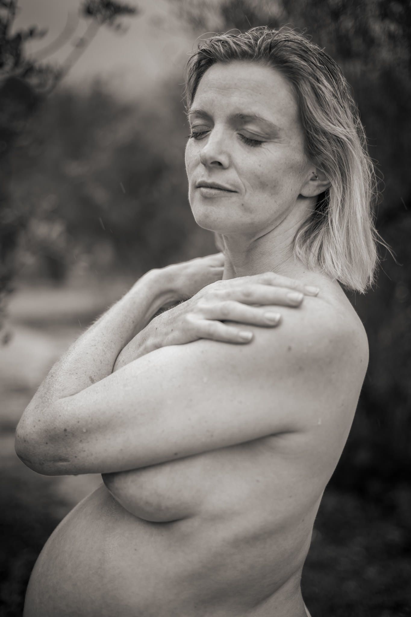 Black and white artistic nude portrait showing peaceful contemplative pose with natural lighting outdoors.