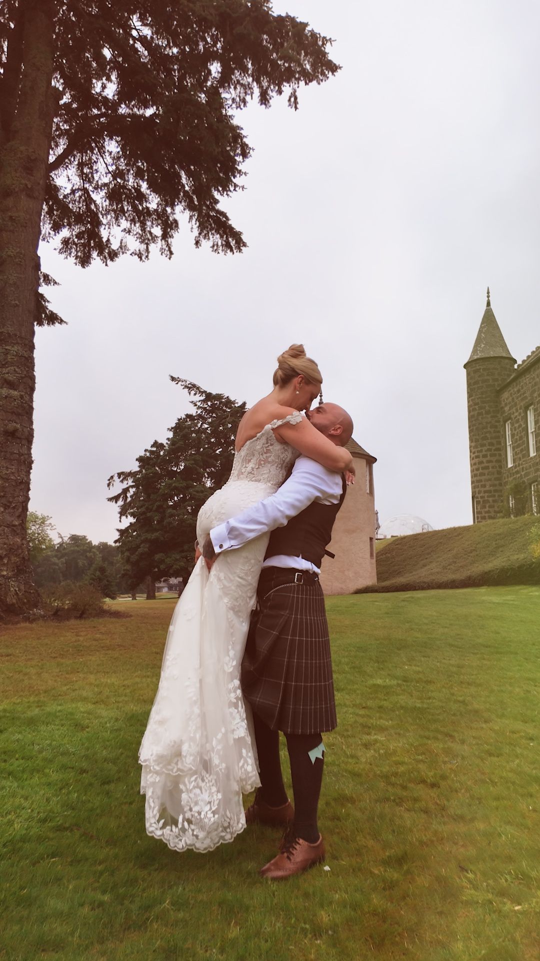 A couple in wedding attire embraces during a romantic dip pose with a Scottish church in the background.