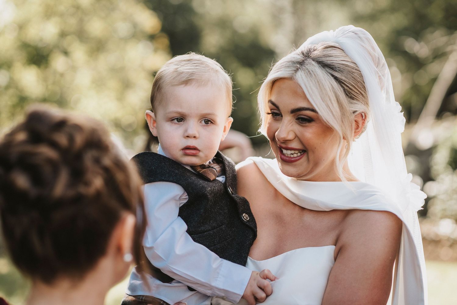 A bride in a white wedding dress shares joyful moments with loved ones during an outdoor celebration.