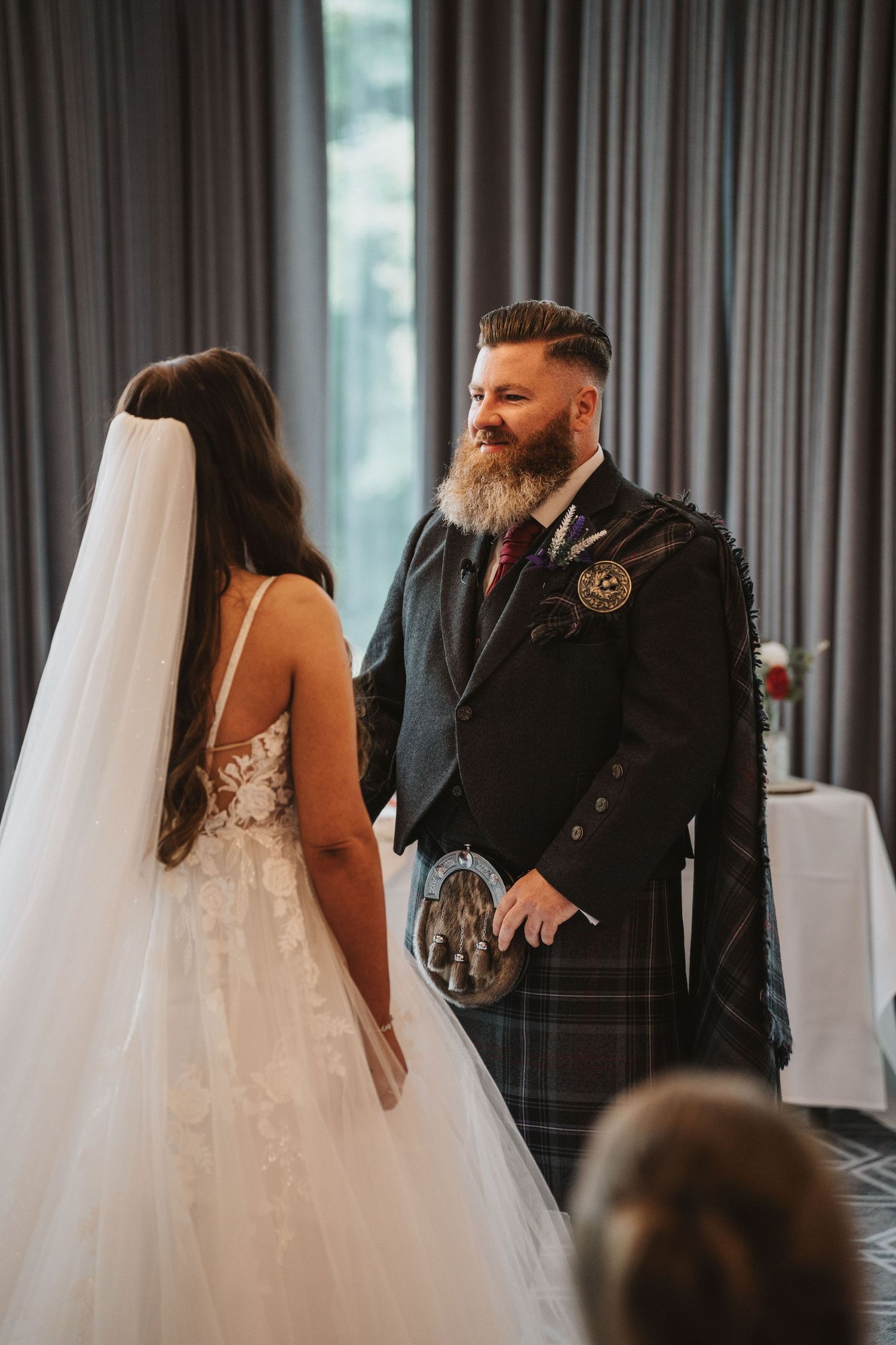 A groom wearing a traditional Scottish kilt faces his bride during their wedding ceremony.
