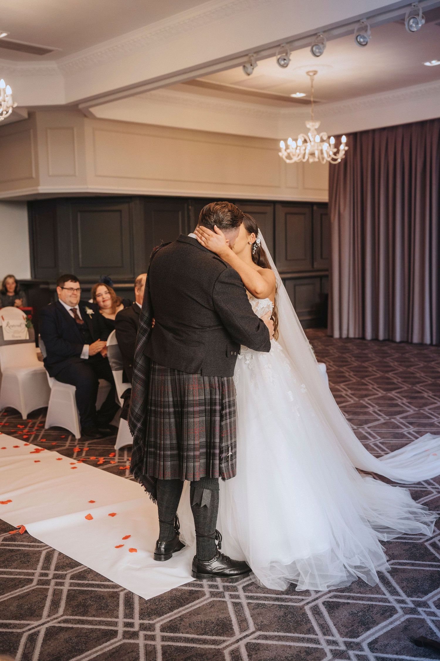 A romantic wedding ceremony with a couple embracing while the groom wears a traditional Scottish kilt and sporran.