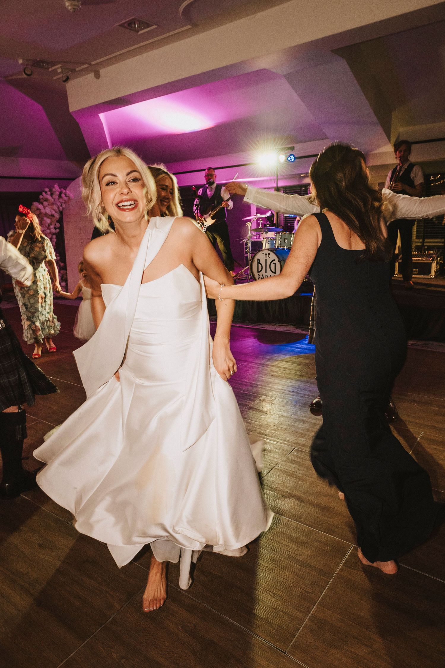 A person in a white dress twirls and dances on a wooden dance floor under purple lighting at an event.