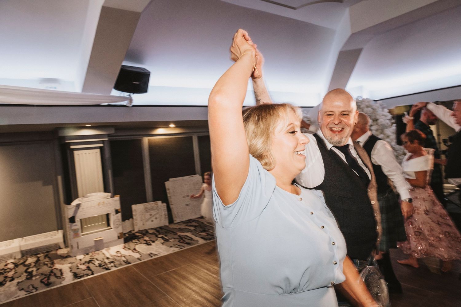 Guests dancing and celebrating at an indoor reception venue with carpeted floors and ambient lighting.