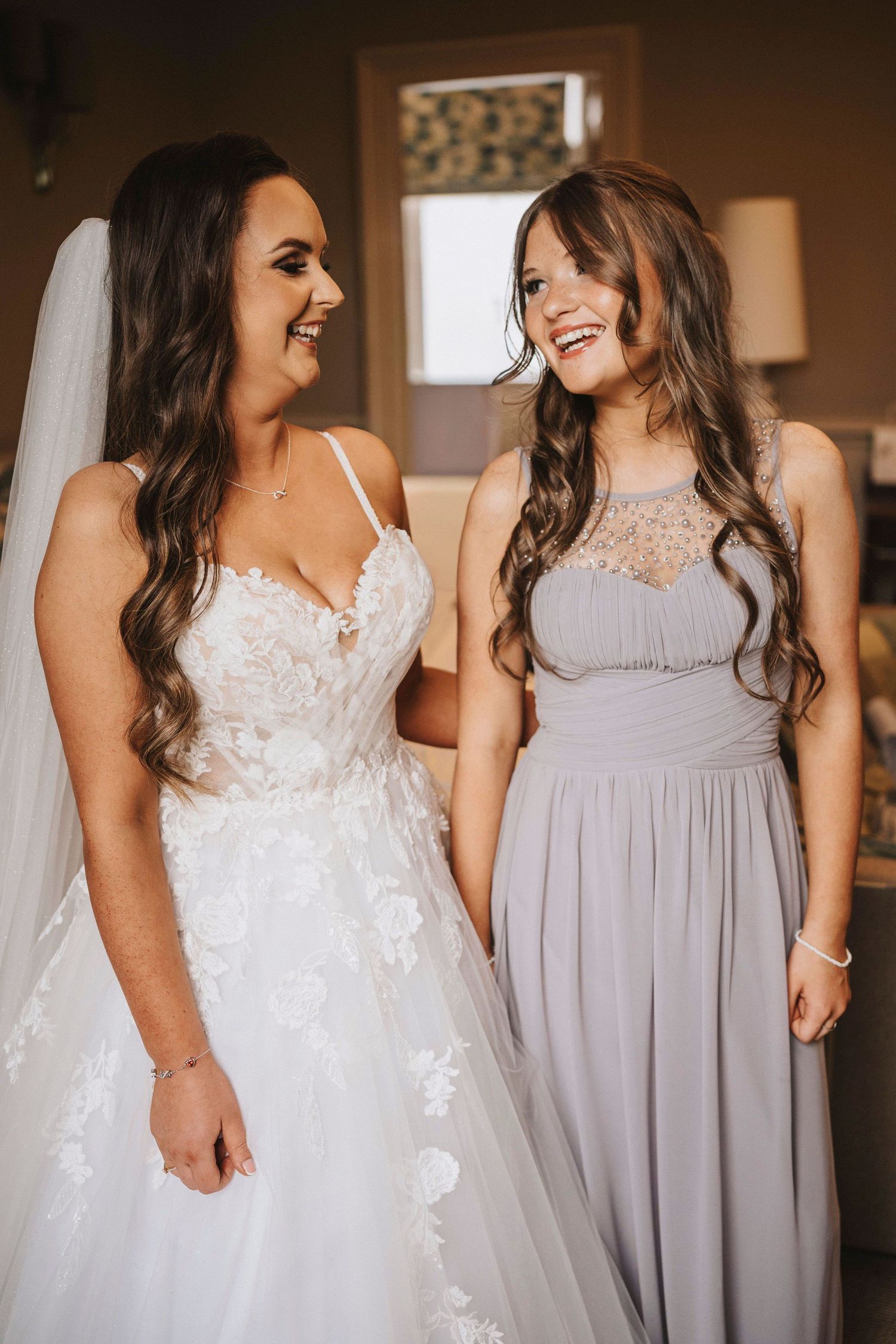 A candid wedding photo showing close up details of a white lace bridal gown and a lavender bridesmaid dress.