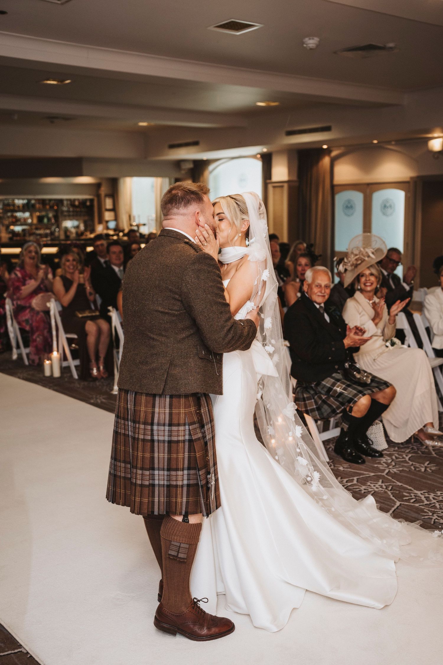 Wedding guests dance together in a ballroom during a reception with Scottish-themed attire and kilts.