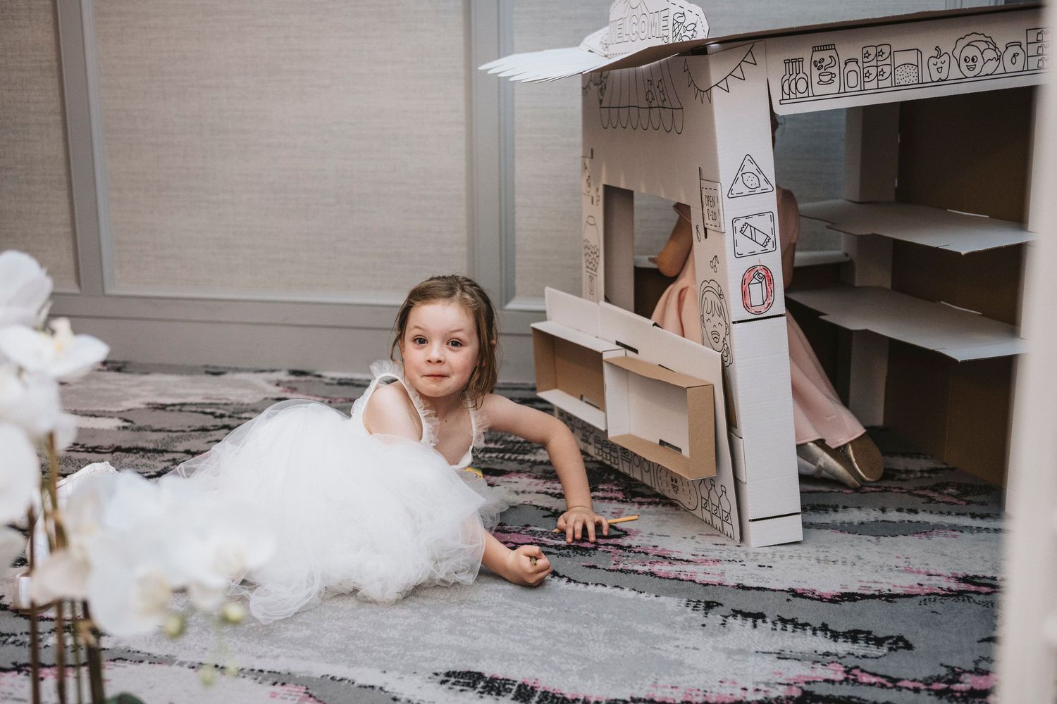 A small child in formal attire crawls playfully on the floor near a wedding dress during a celebration.