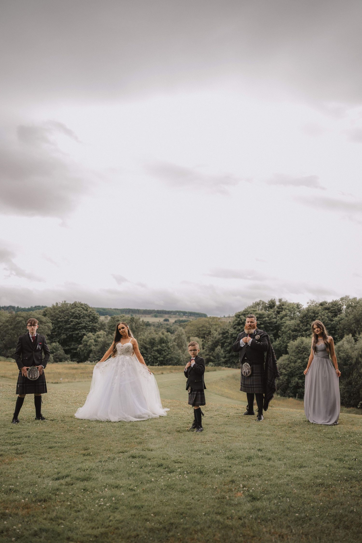 Wedding party spaced apart on green hillside for creative portrait composition.