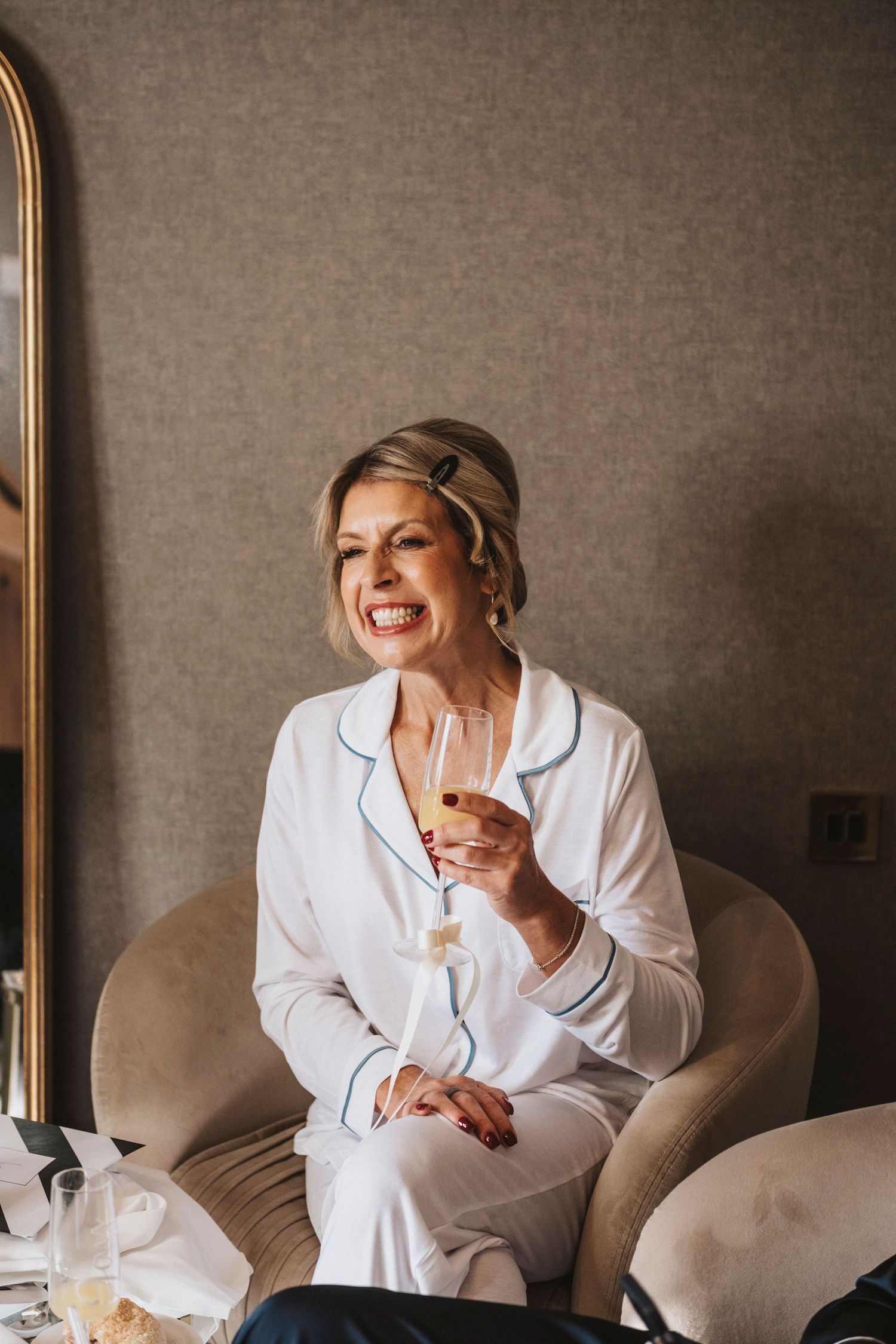 A person in white spa robe sits comfortably on beige couch while laughing and enjoying a relaxing moment.