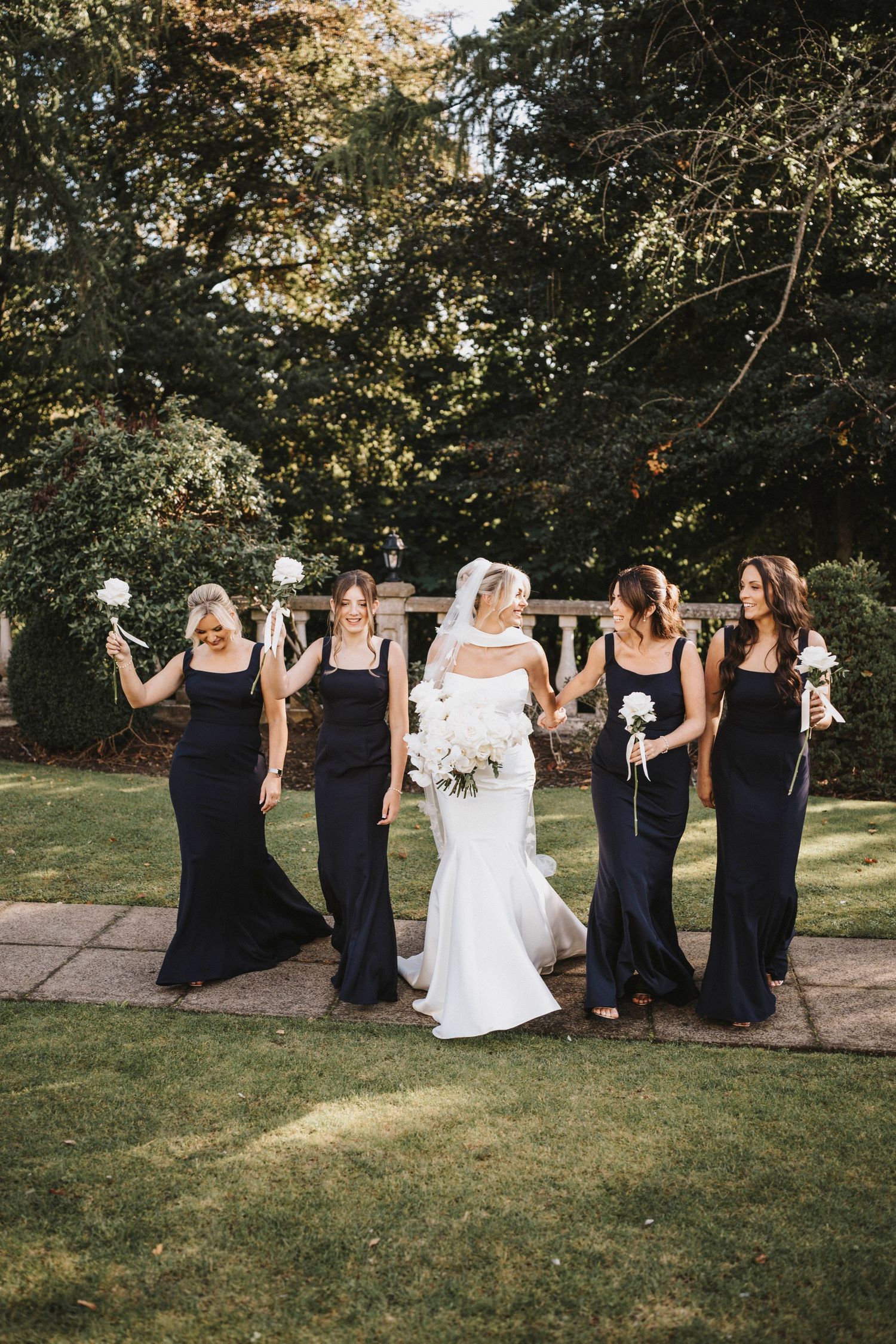Wedding party in navy blue dresses and white gown pose playfully in a sequence of outdoor garden photos.