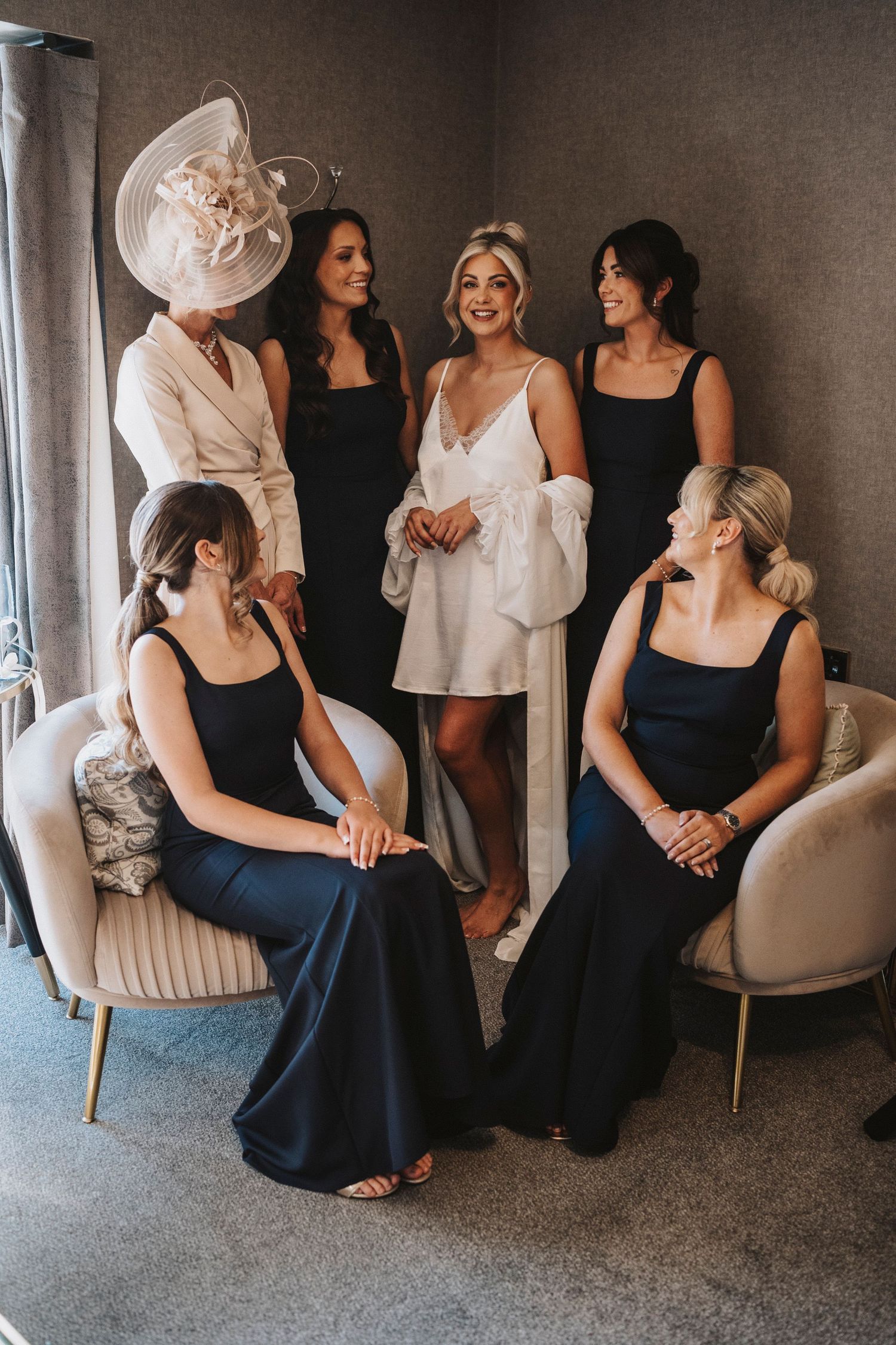 A group of women in black and white dresses sit together in elegant chairs during a formal event.