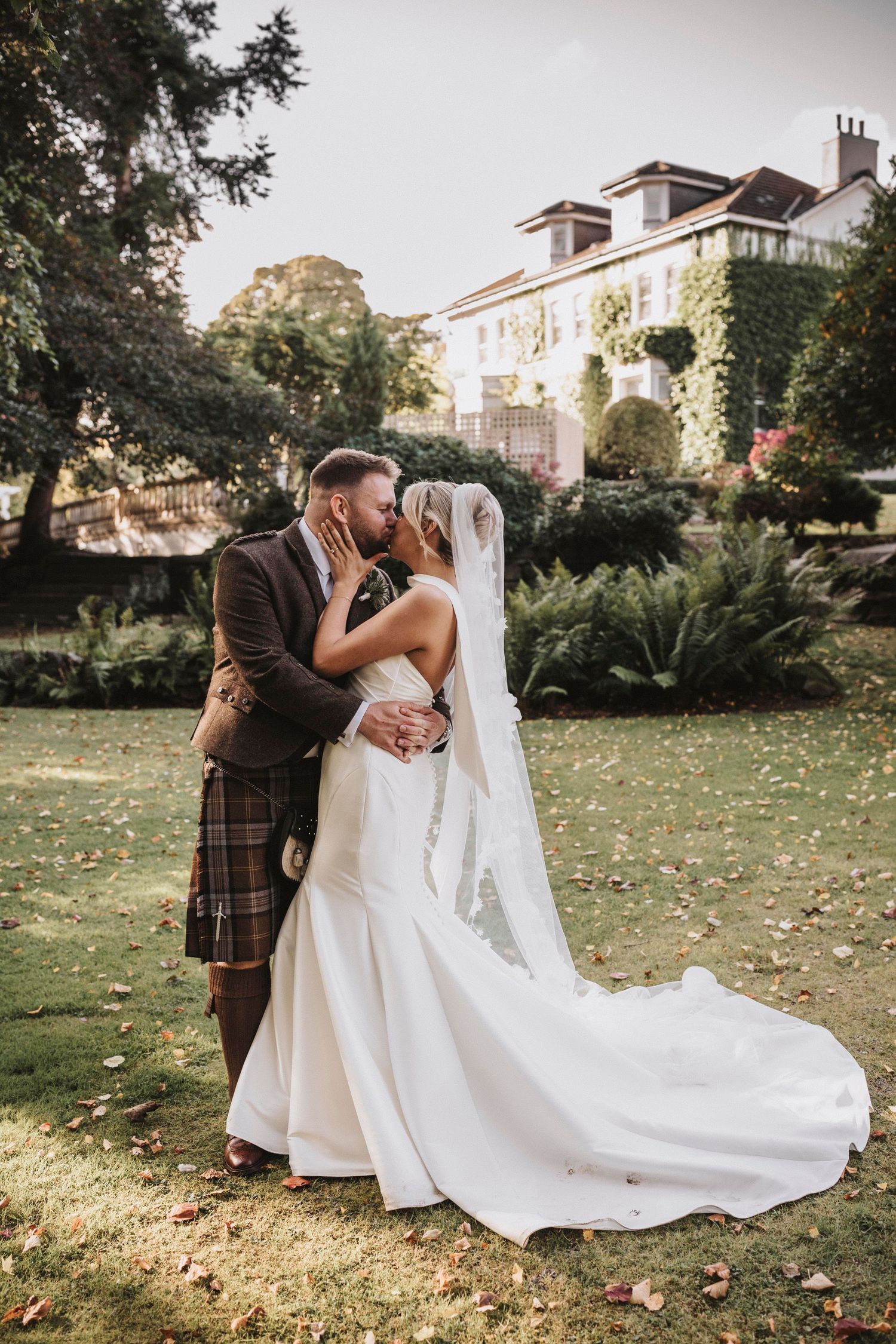 A romantic wedding scene with a bride in a flowing white gown and groom in a plaid suit captured in a garden setting.