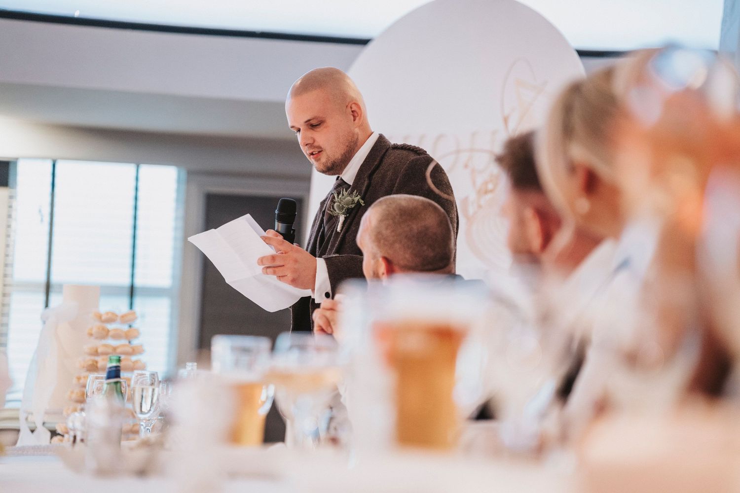 A chef in a black jacket prepares food at a modern restaurant counter while customers watch from their seats.
