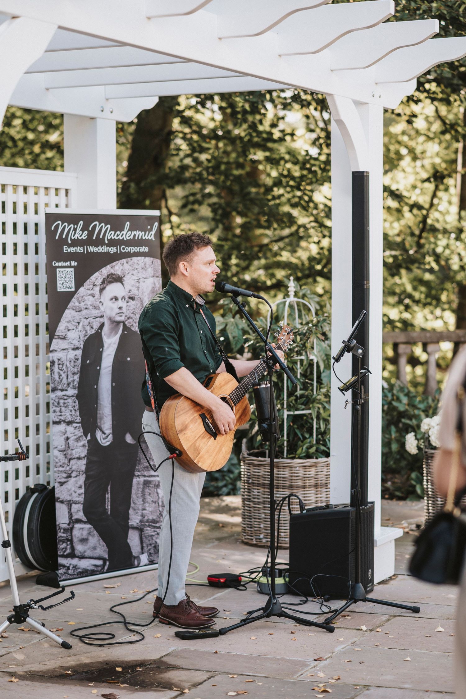 A musician performs with an acoustic guitar on an outdoor stage with white lattice backdrop.