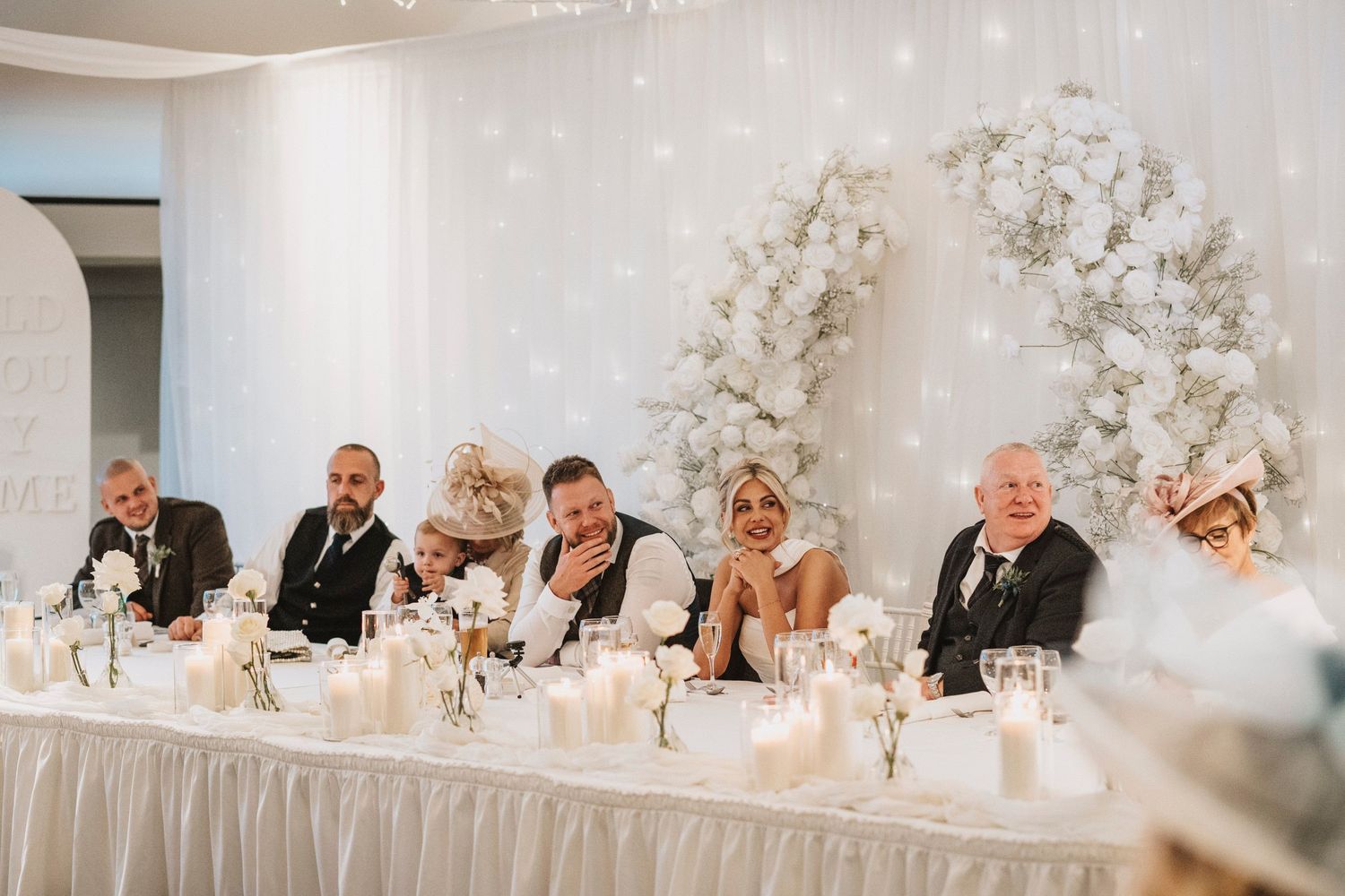 Wedding reception banquet hall decorated with white floral arrangements and elegant table settings for guests.