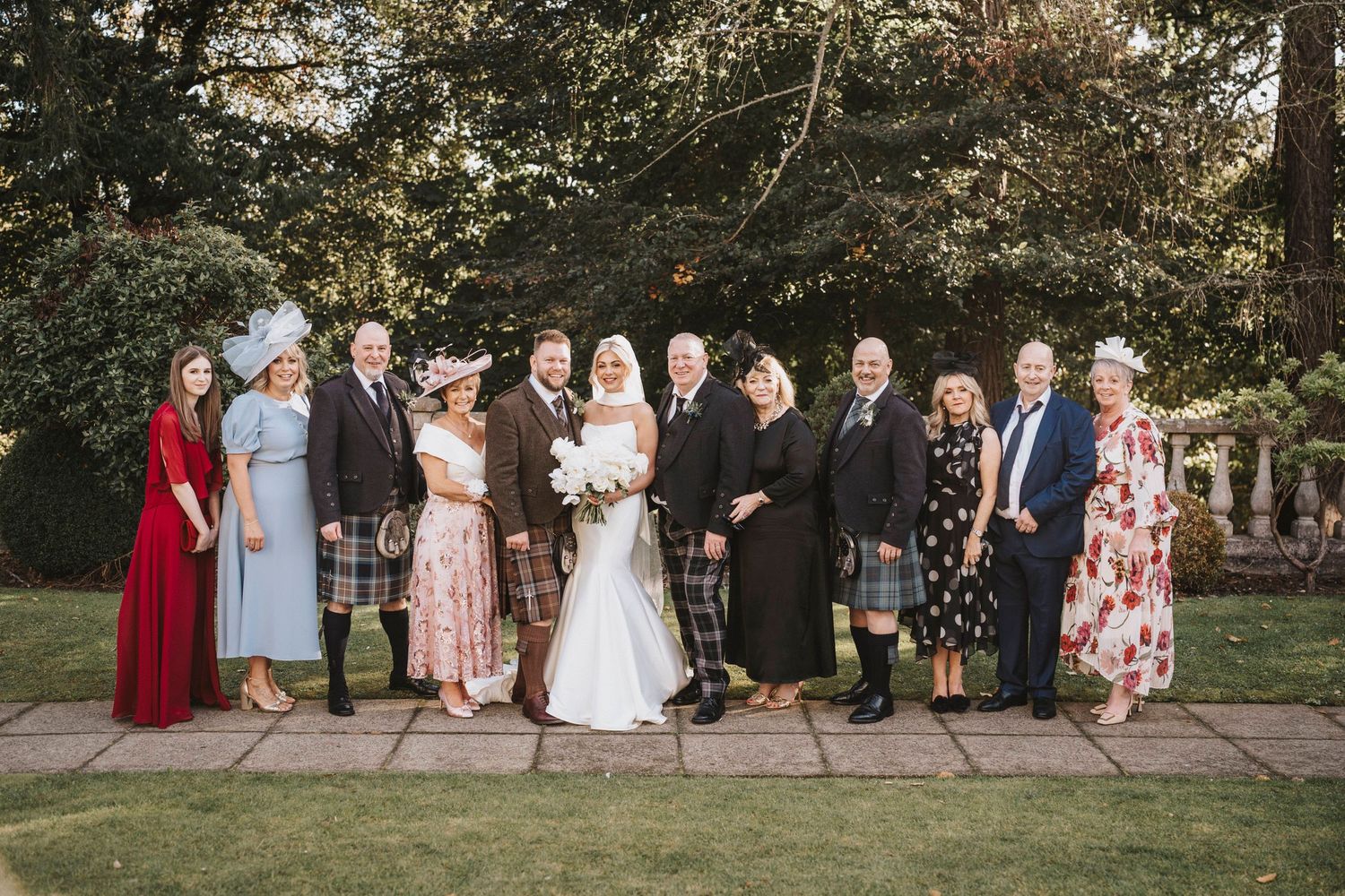 Wedding party members gather outdoors for formal group photos in a garden setting.
