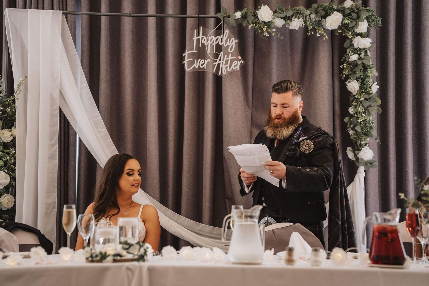 Wedding reception venue setup with floral arrangements and elegant white drapes hanging from ceiling.