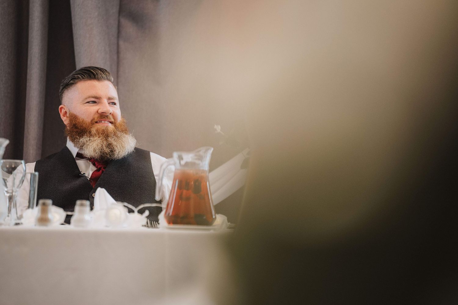 Bearded person sitting at table with blurred lighting and soft focus bokeh effect in foreground.
