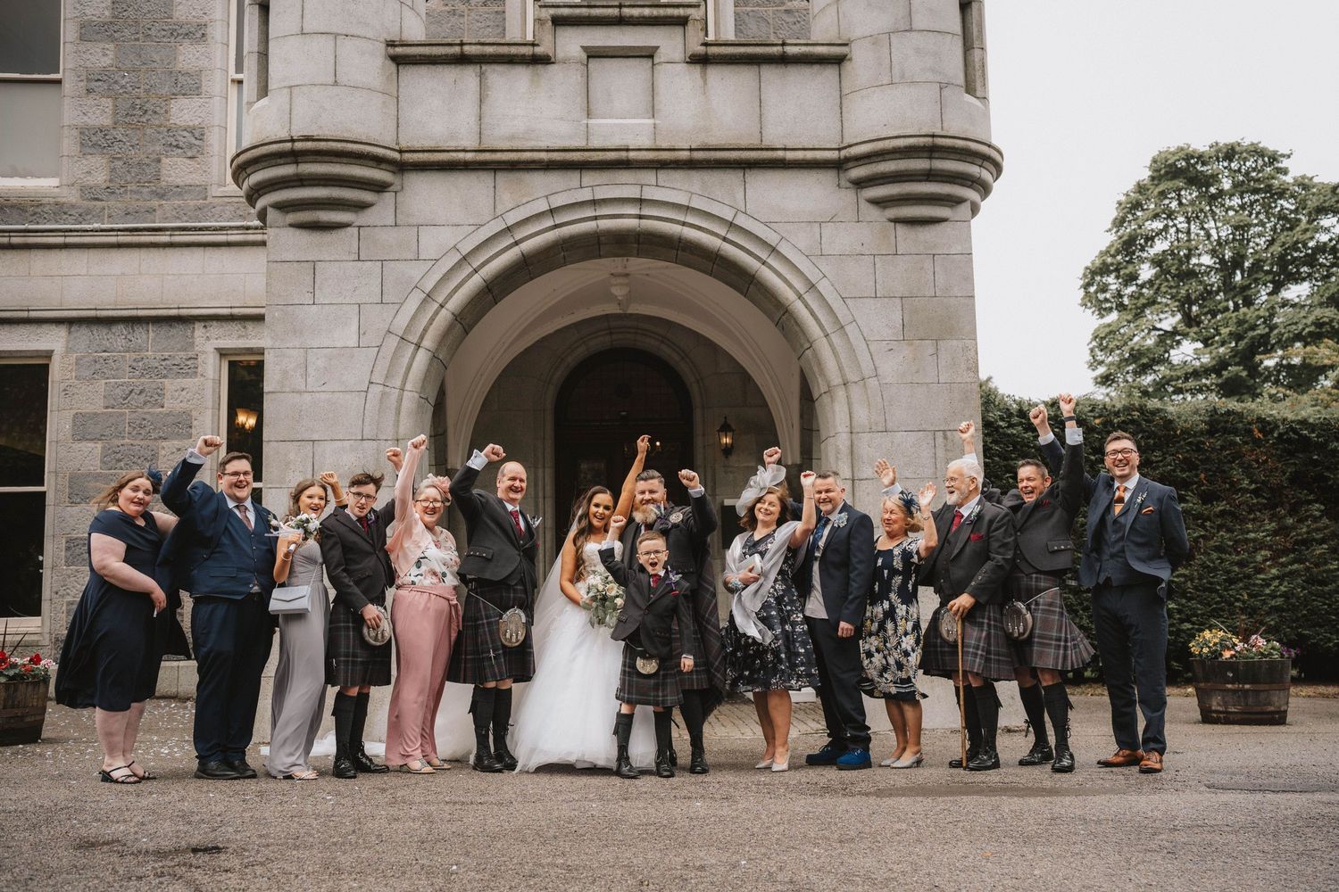 Wedding guests line up outside a grand stone archway entrance of a historic building for the receiving line.