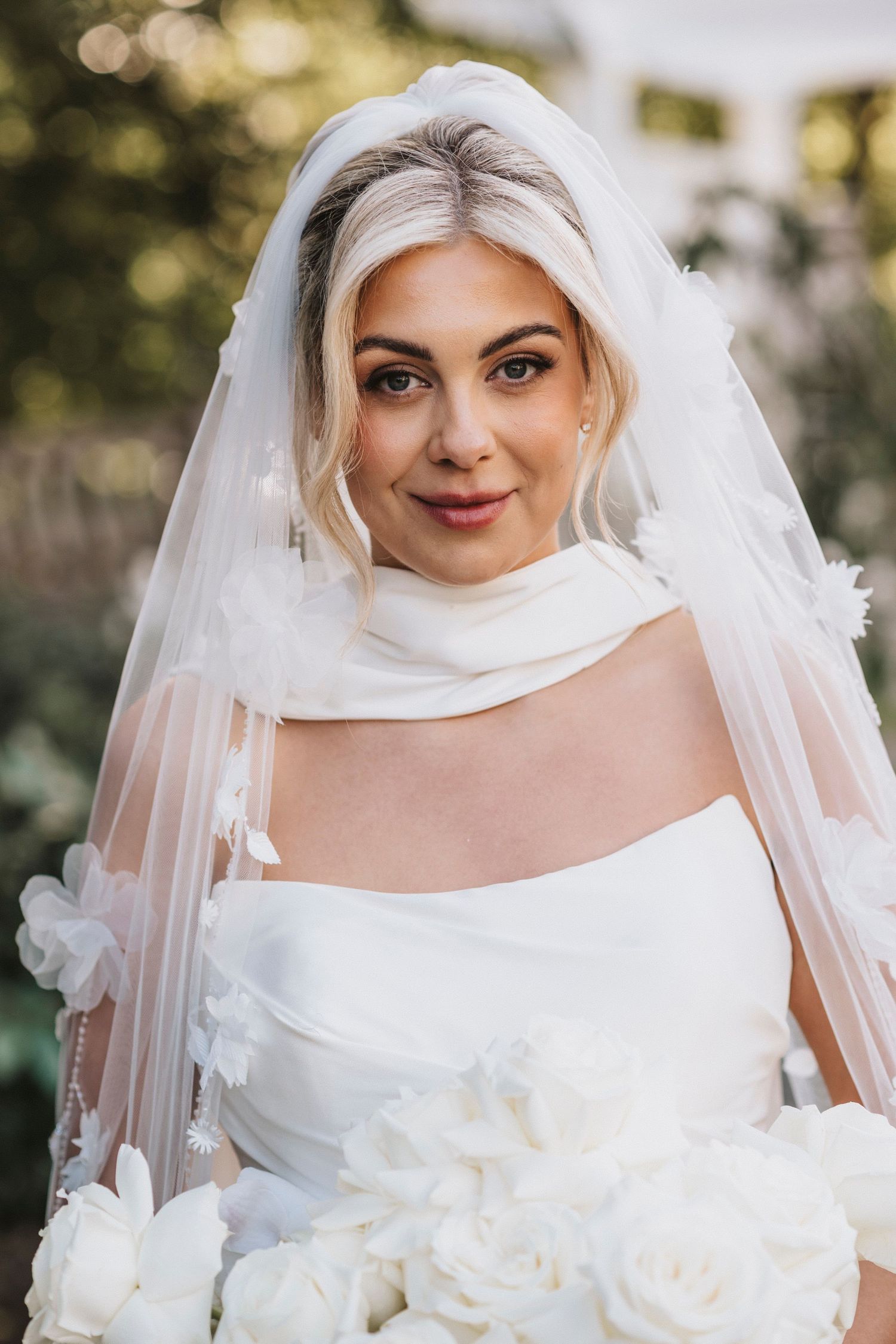 A bride in a classic white wedding gown and veil poses for a series of close-up portraits outdoors with bokeh lighting effects.