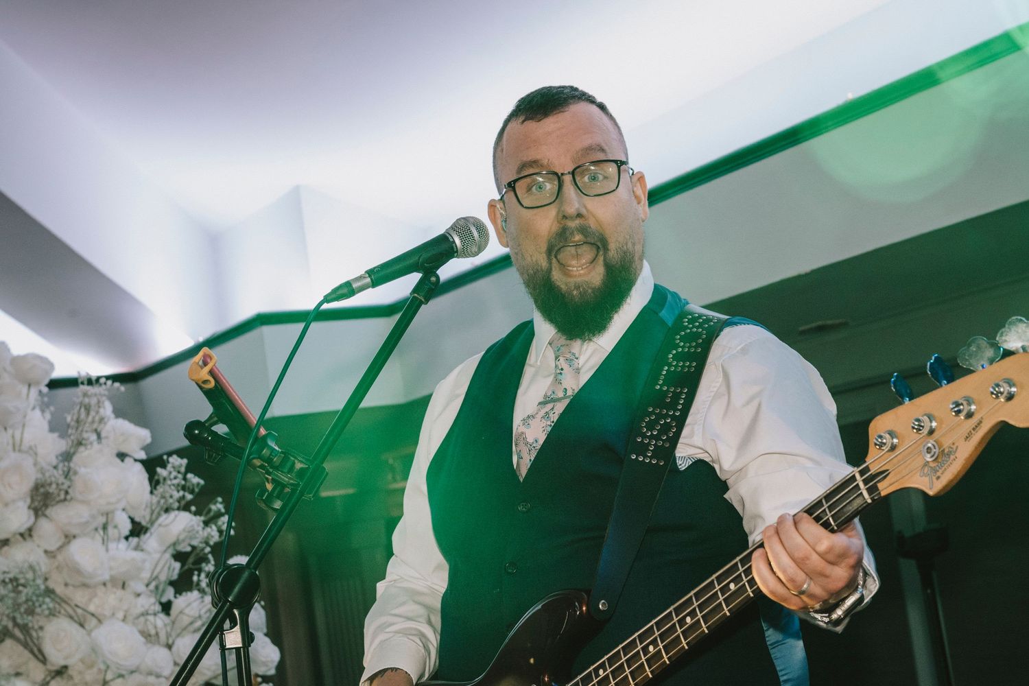 Bass player in a green vest performing with a guitar at an event with decorative lighting.