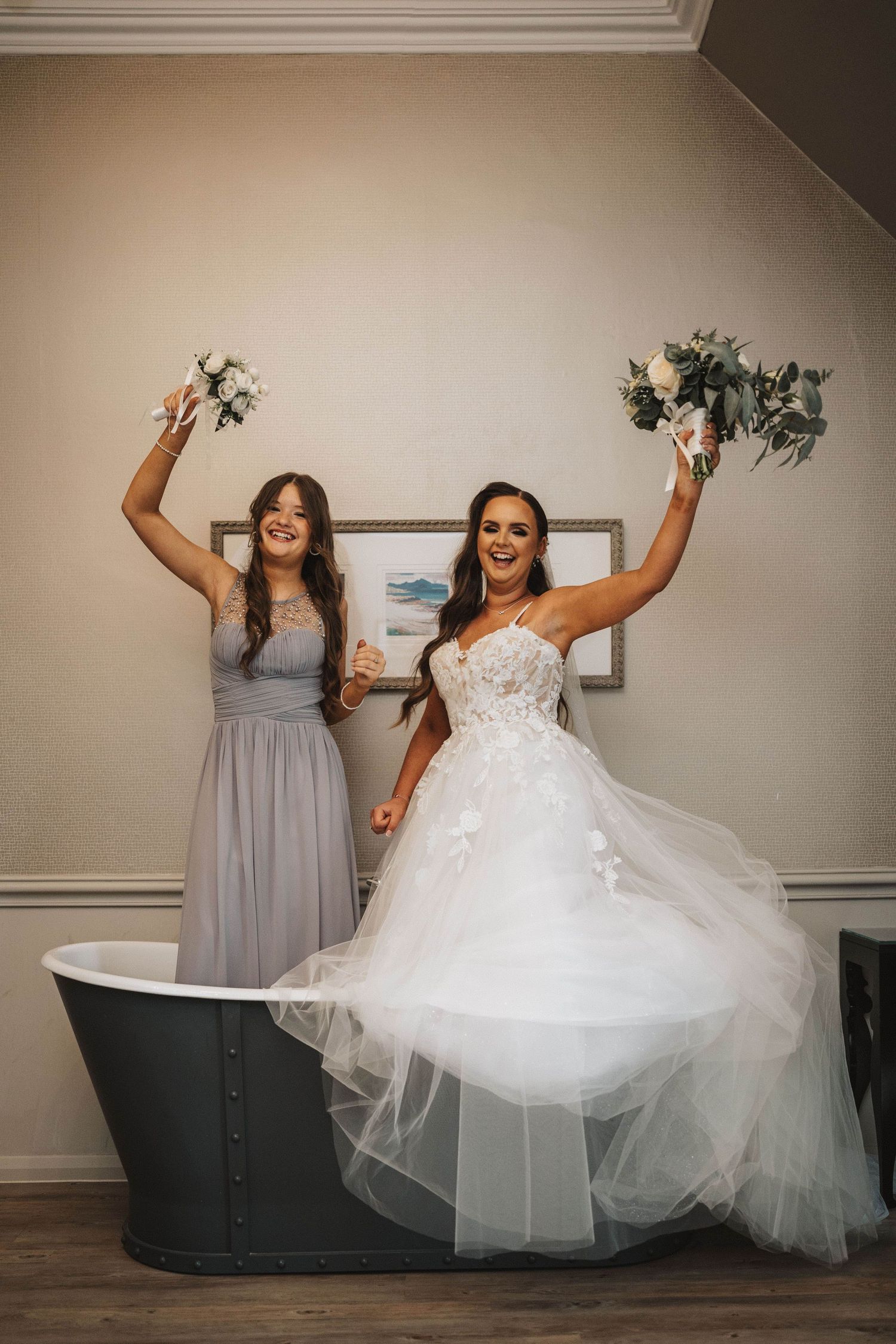 A group poses playfully in a room showing off a flowing wedding gown and gray bridesmaid dresses.