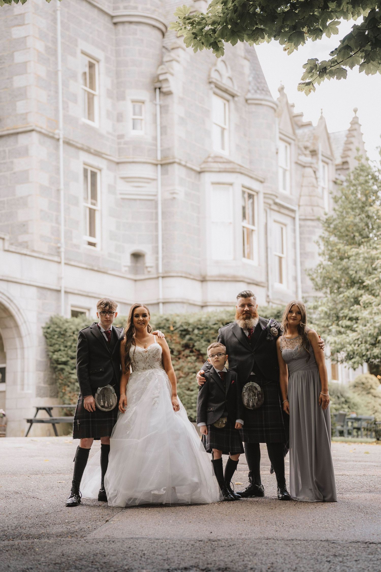 Wedding party poses for photos in front of a grand stone castle building.