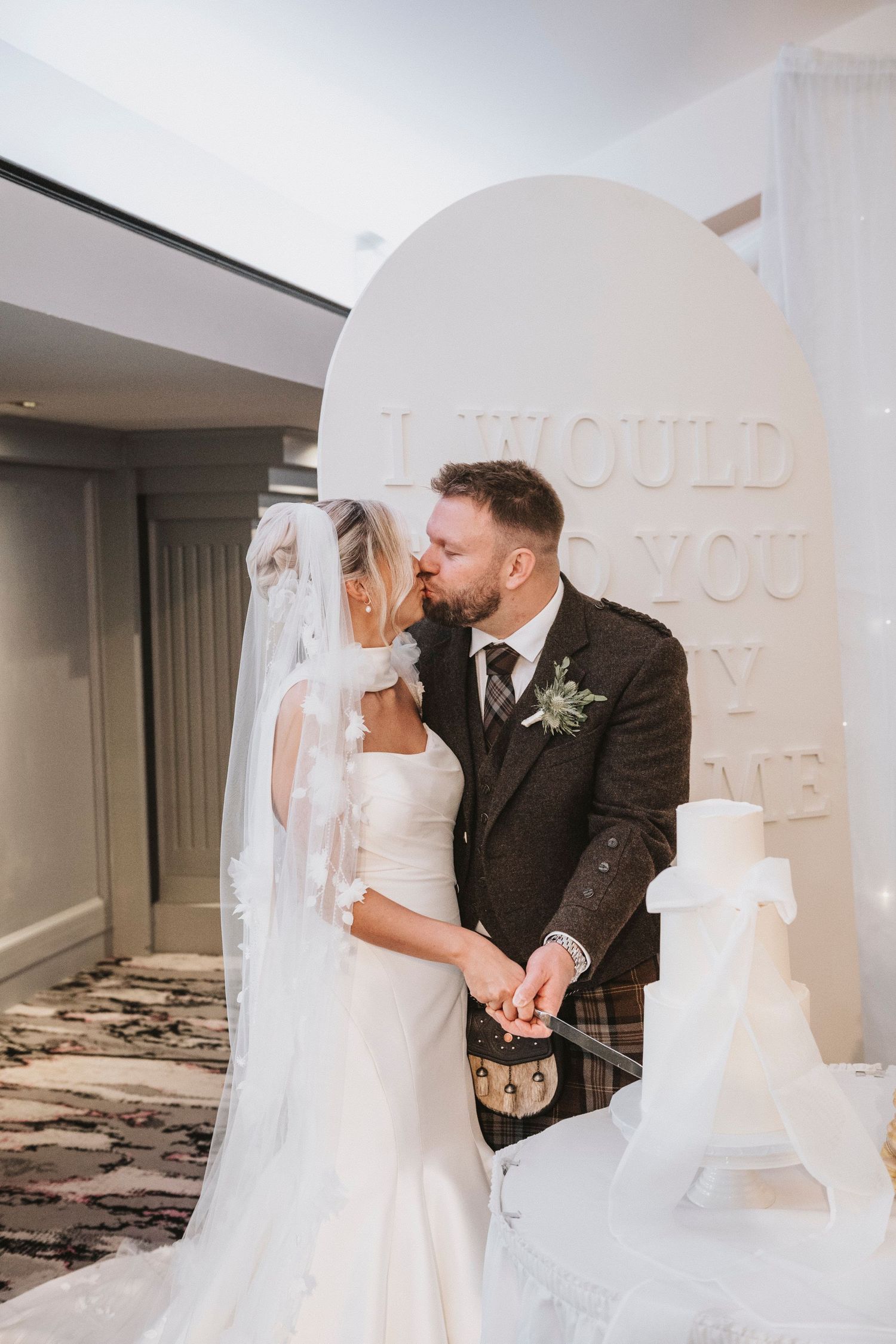 Bride and groom share a sweet moment while cutting their elegant white wedding cake at their reception.