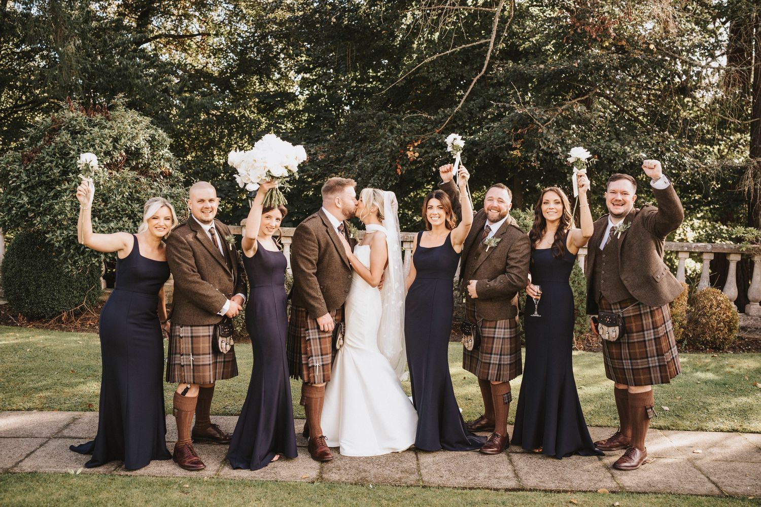 Wedding party wearing brown and navy outfits poses together on garden steps for formal group photos.