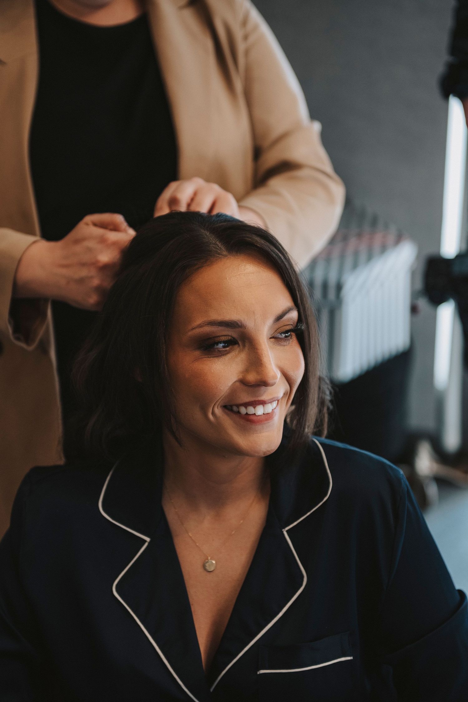 A person in a dark blazer with white trim smiles warmly while looking to the side in a professional setting.