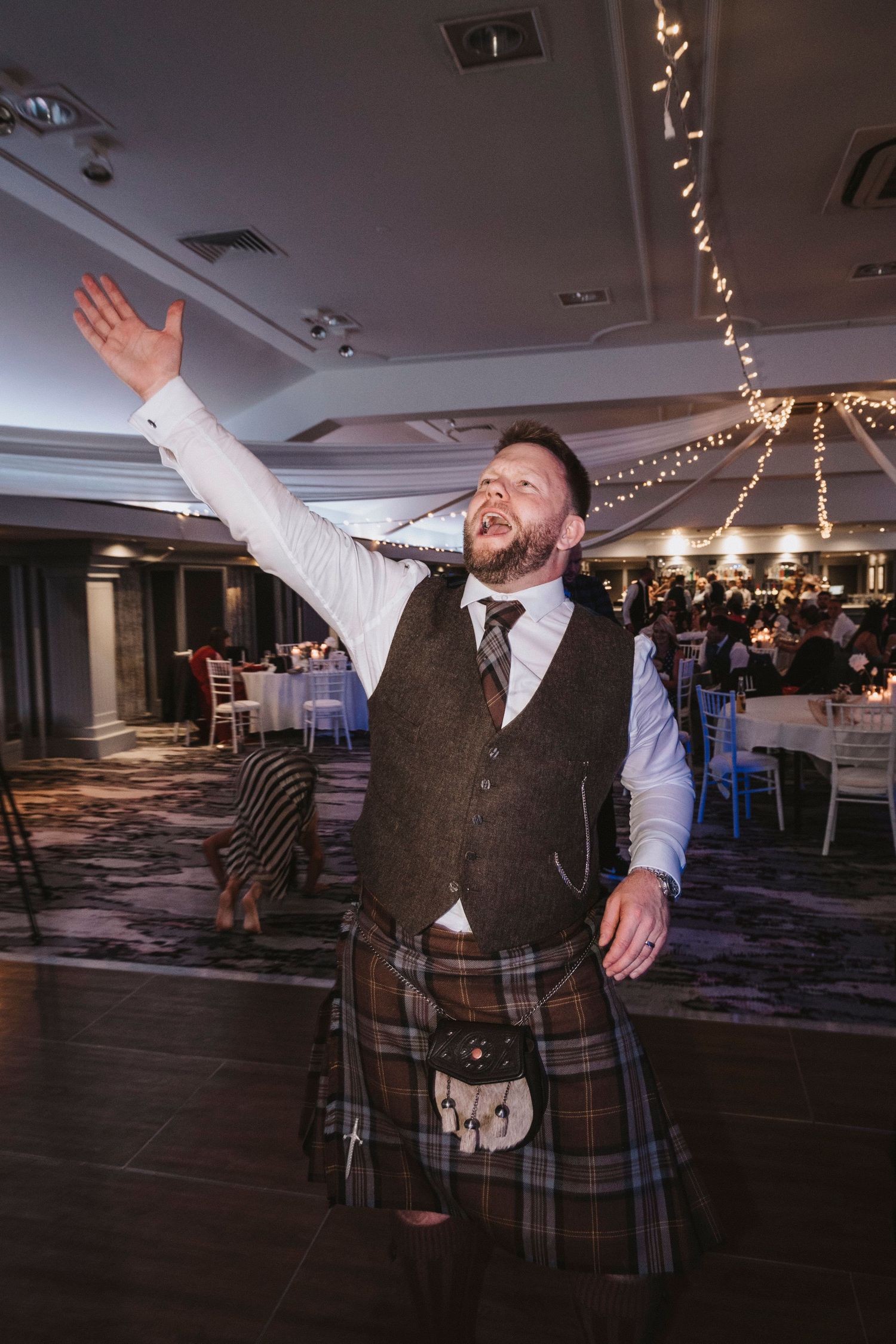 A sequence of photos showing a person in a kilt and vest dancing enthusiastically at an indoor event venue.