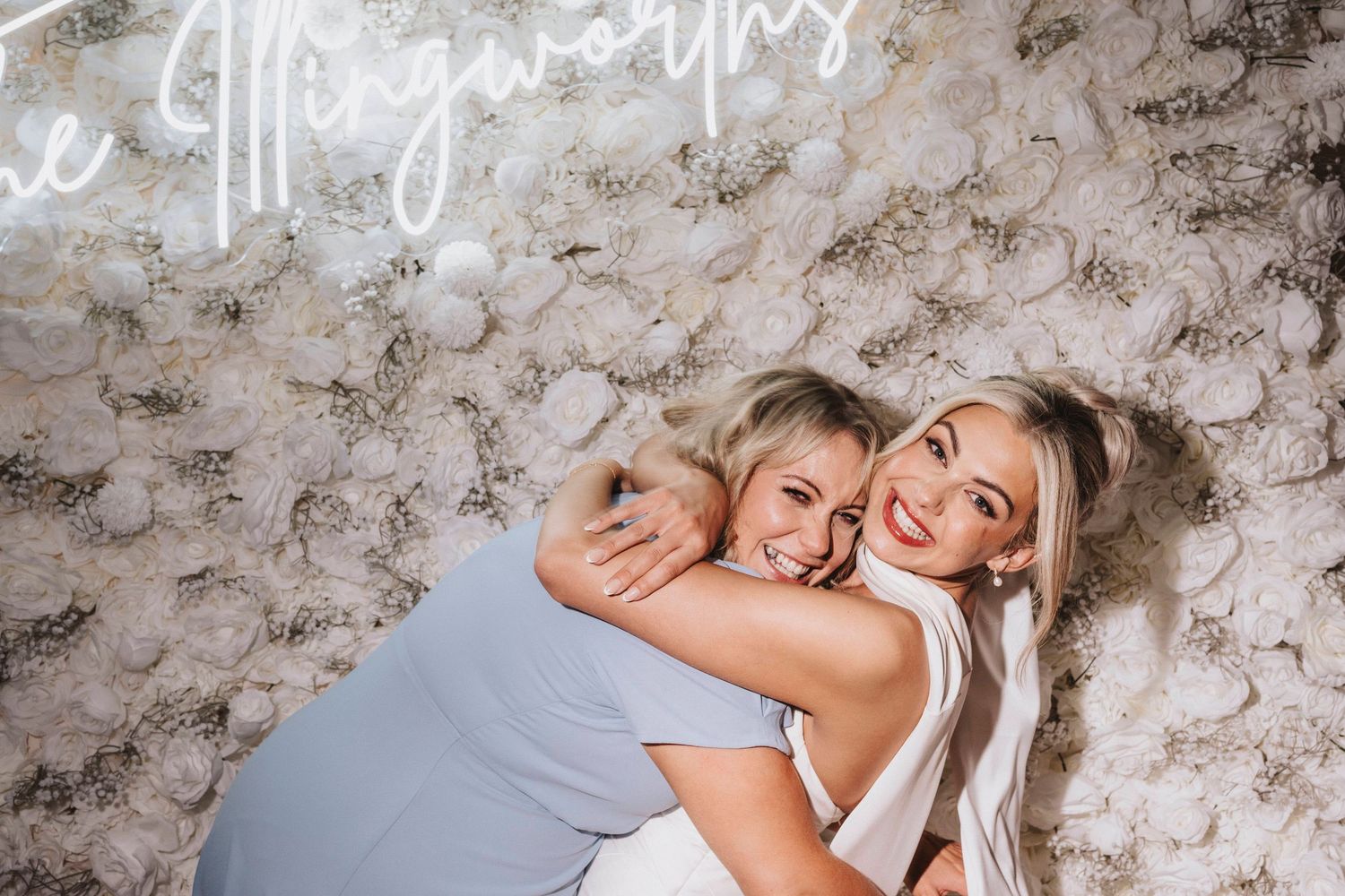 Women sharing joyful hugs and laughter during a celebration with decorative wall background.