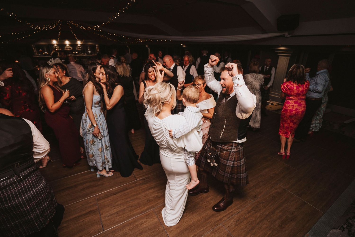Wedding guests dance and celebrate on a dimly lit dance floor during an evening reception.