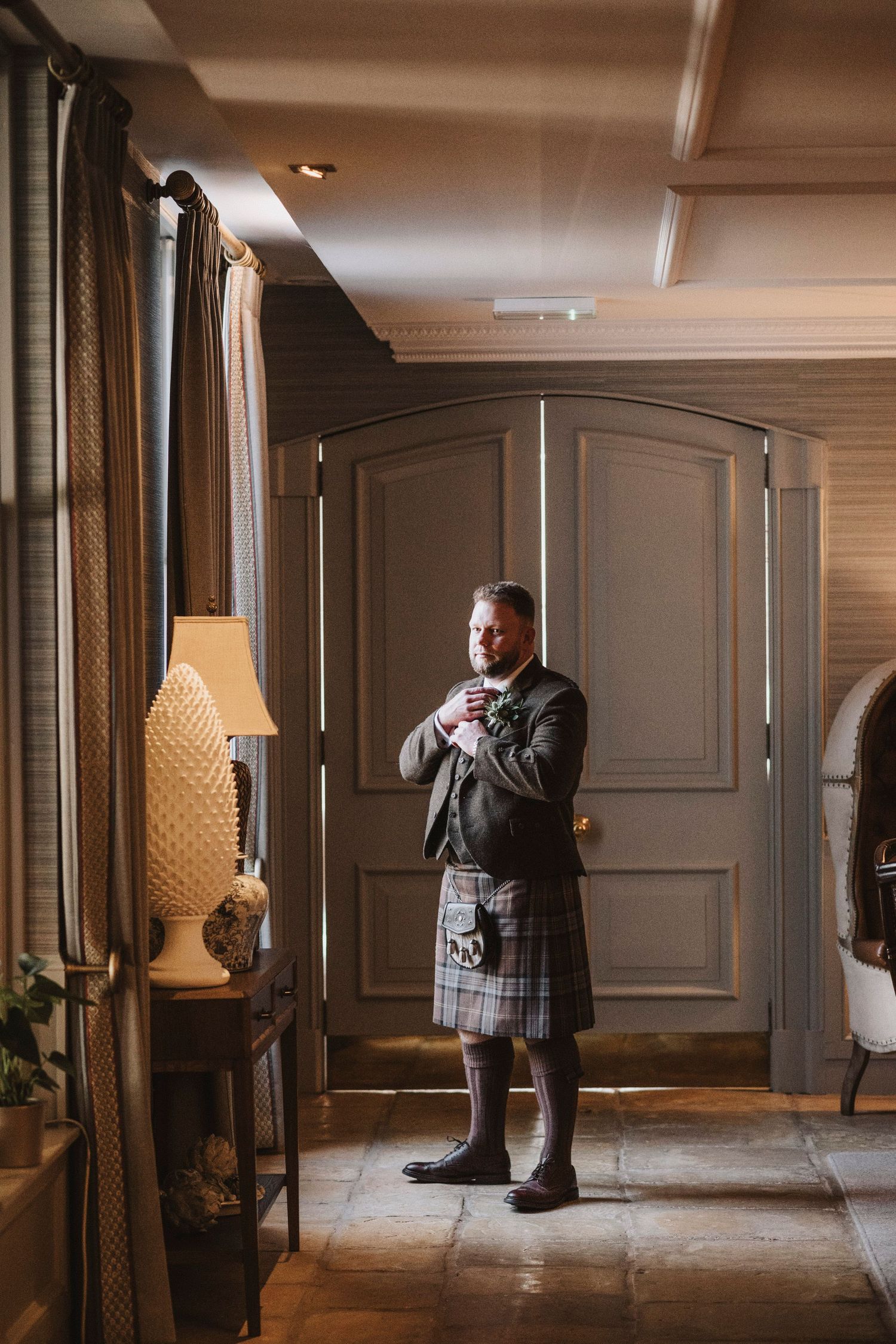 A person wearing a kilt stands in an elegant hallway with wooden paneling and ornate decor.